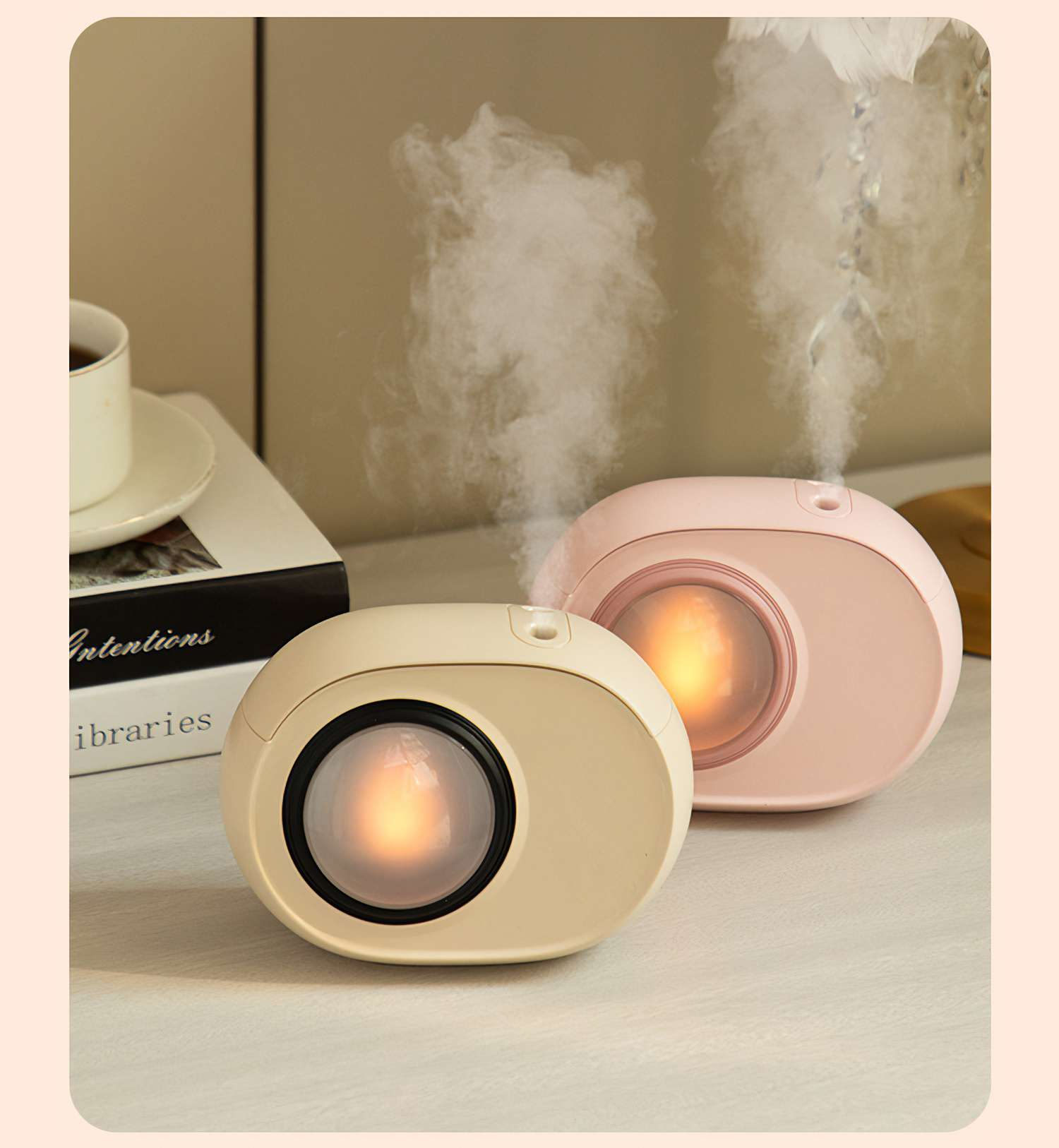 Zwei ovale Luftbefeuchter, einer beige, einer rosa, die Dampf abgeben. Ein Buch und eine Tasse sind im Hintergrund.