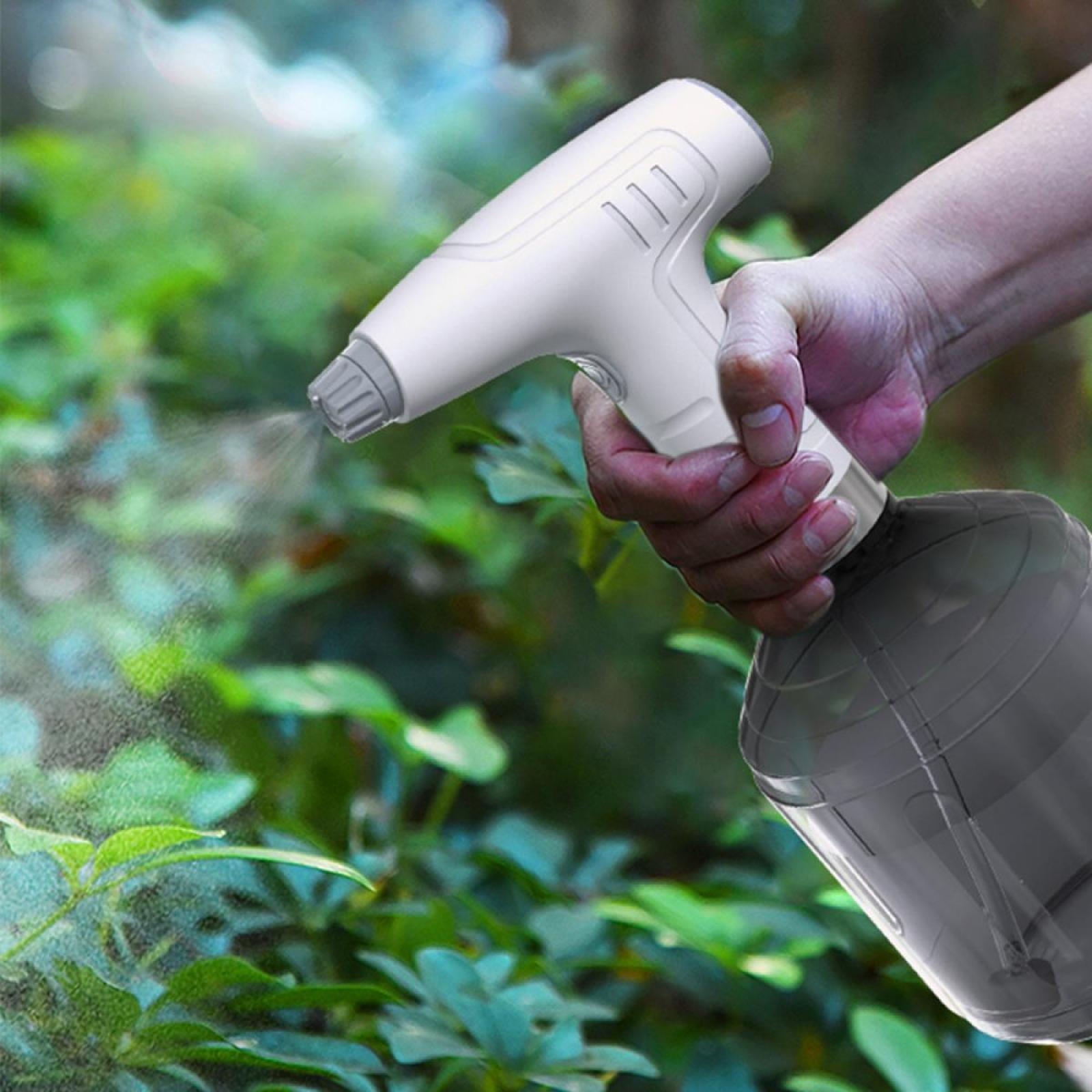 Hand hält eine weiße Sprühflasche und sprüht Wasser über grüne Pflanzen in einem Garten.