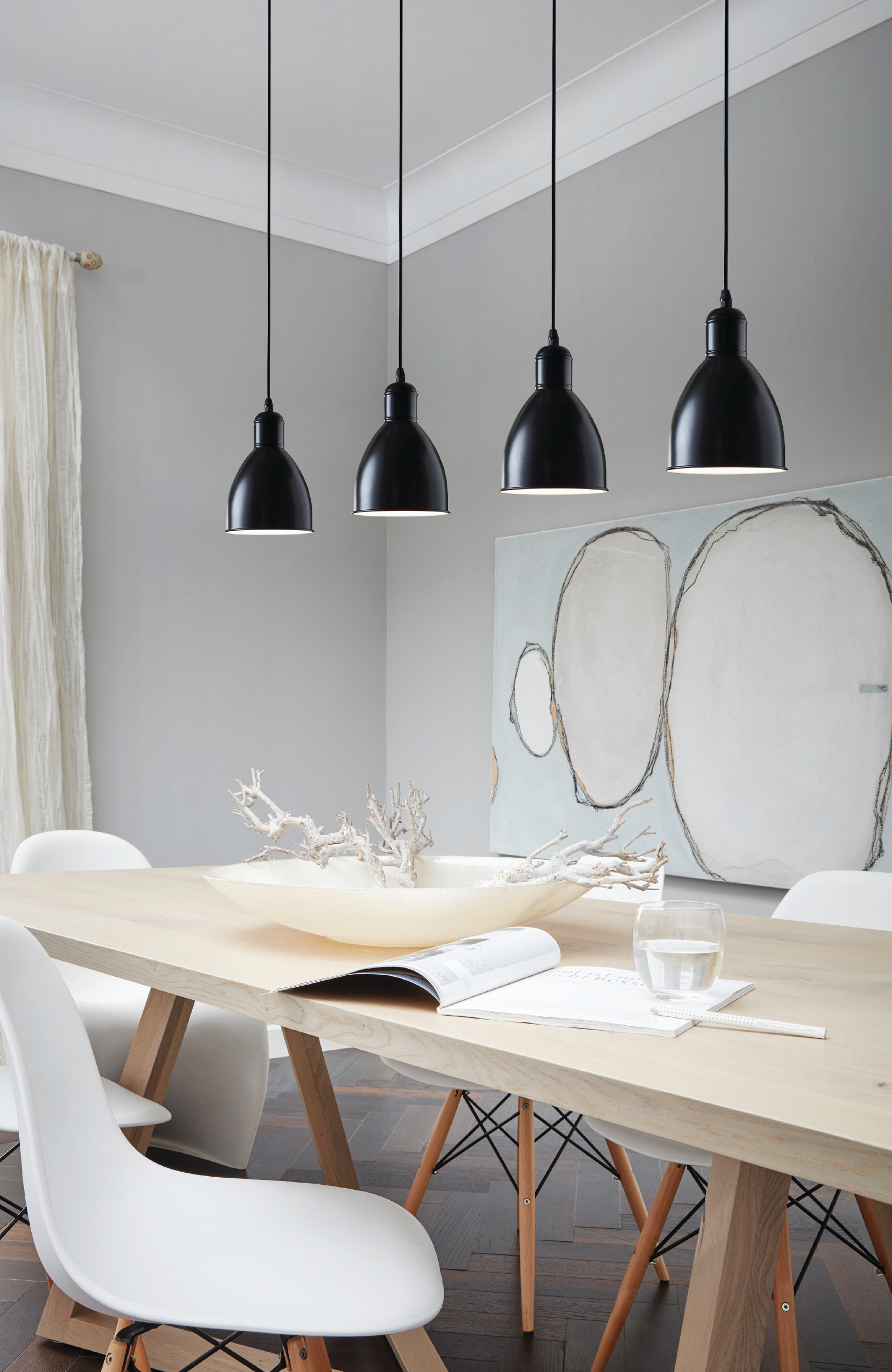 Jadalnia ze stołem, krzesłami i czterema czarnymi lampami wiszącymi. Na ścianie wisi obraz. Na stole stoi miska z gałęziami.