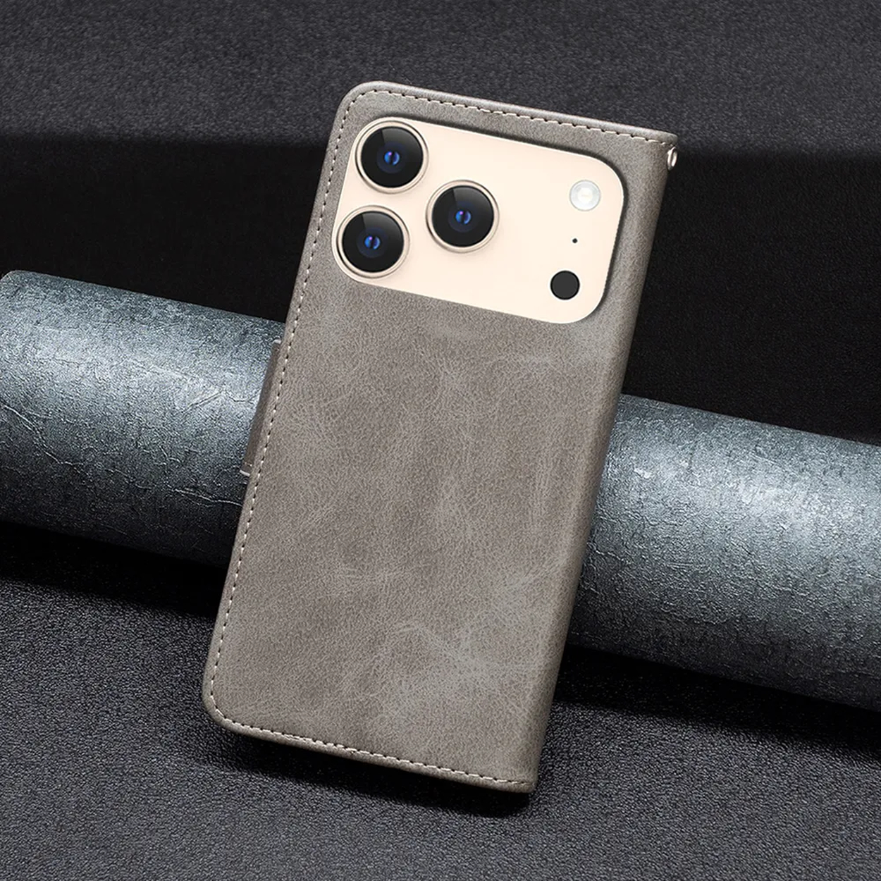 Een grijze telefoonhoes met cameralenzen ligt op een donker, getextureerd oppervlak. De hoes is leerachtig en de achtergrond is metallic.