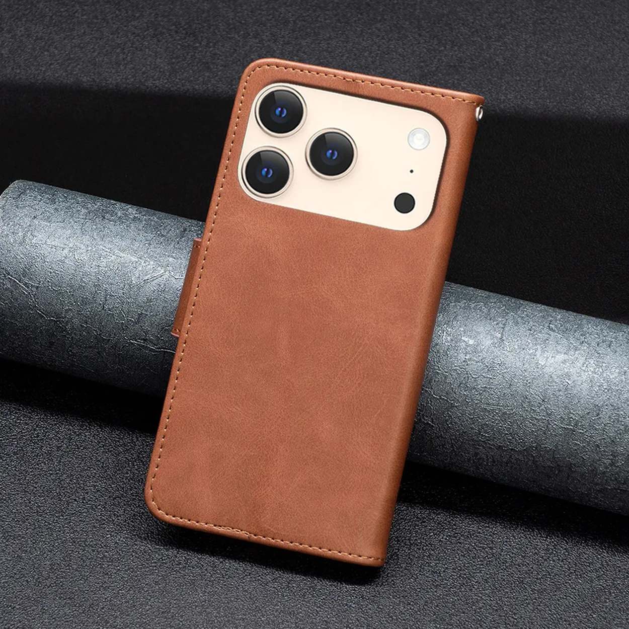 Bruine leren telefoonhoes met drie cameralenzen. De hoes ligt op een grijs oppervlak met textuur tegen een zwarte achtergrond.