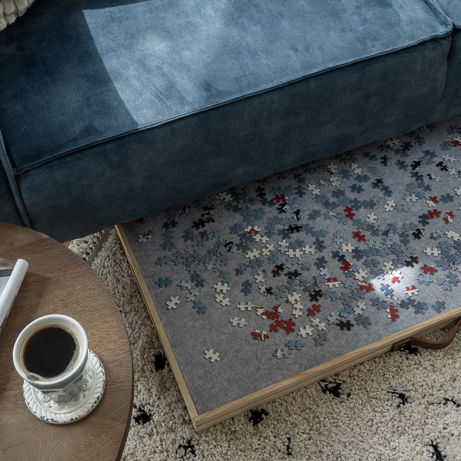A partially completed jigsaw puzzle on a gray felt mat. A cup of coffee sits on a table next to a blue sofa.