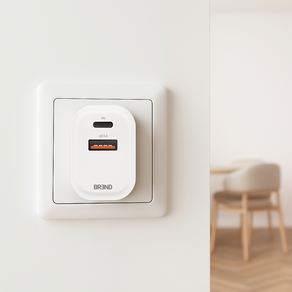Une prise murale blanche avec un chargeur blanc branché. Le chargeur a un port USB noir et un port QC3.0 orange. Un arrière-plan flou montre une chaise.