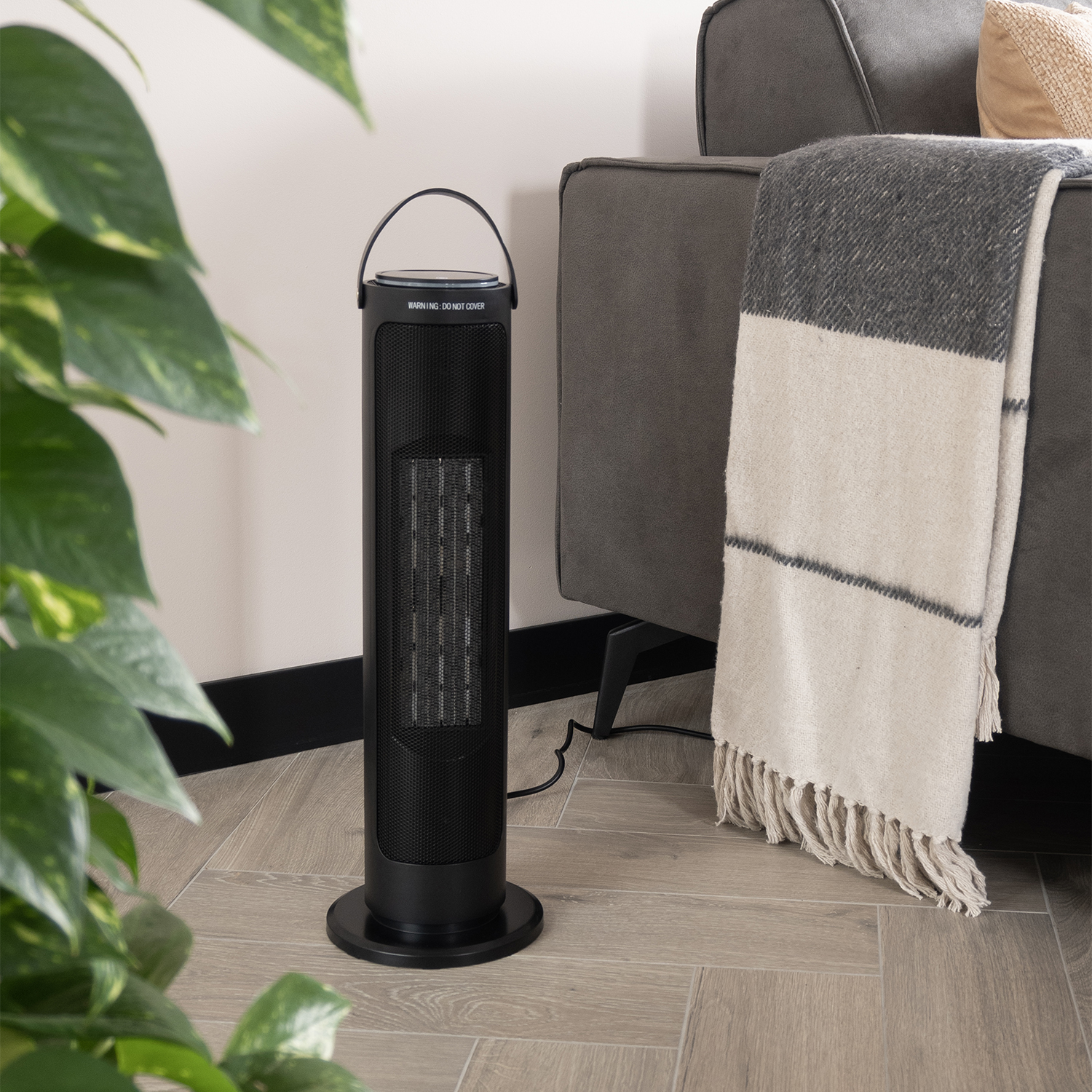 A black space heater stands next to a grey couch with a blanket. A green plant is in the foreground.