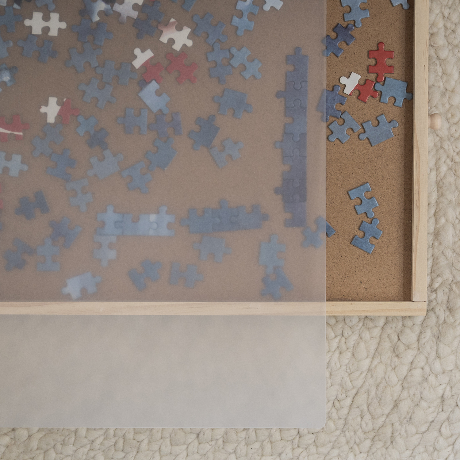 A puzzle in a wooden tray. Many puzzle pieces are blue, some white and red. The tray is on a textured, off-white surface.