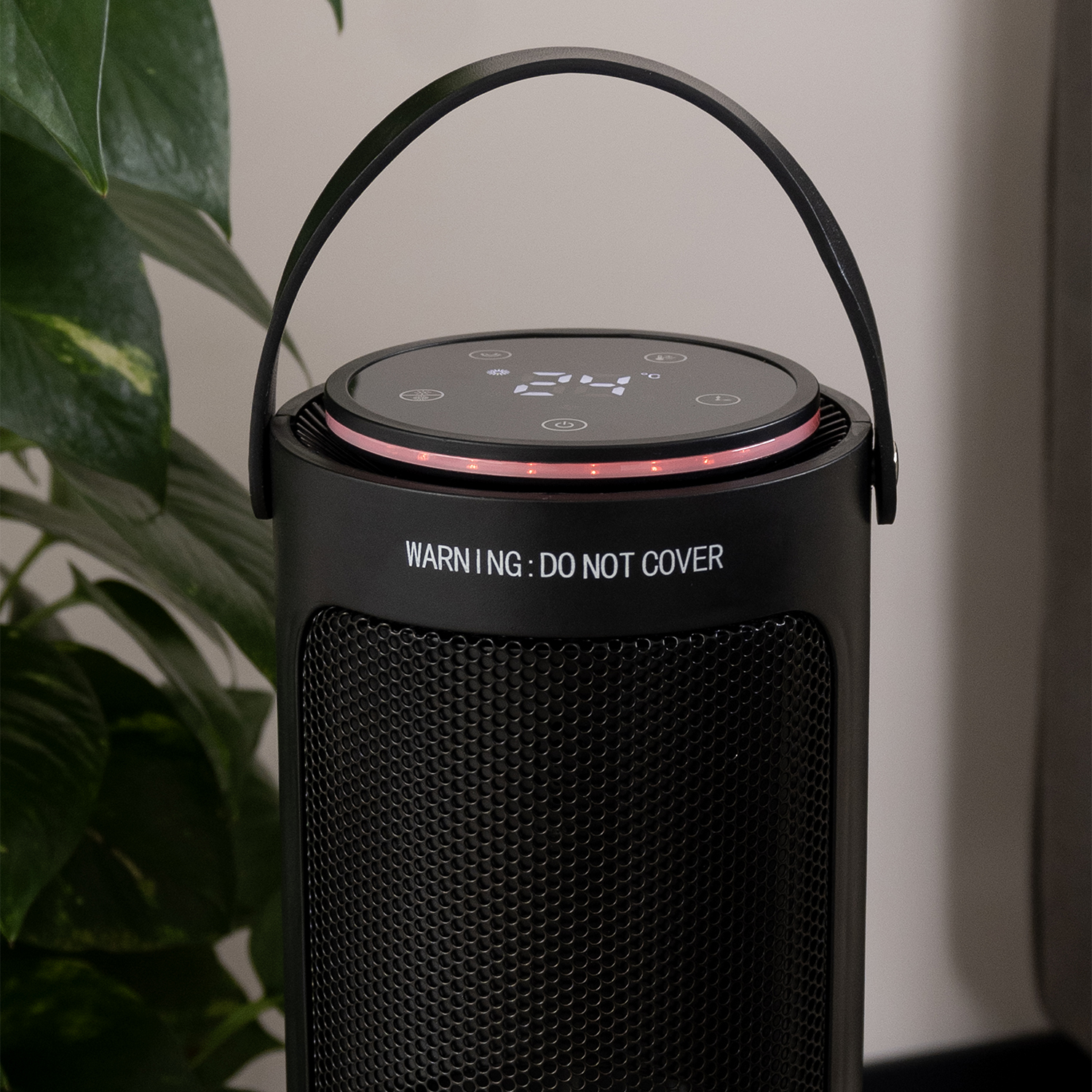 Black electric heater with a handle, digital display showing 24, and red light. Warning: Do not cover. Green plant in the background.