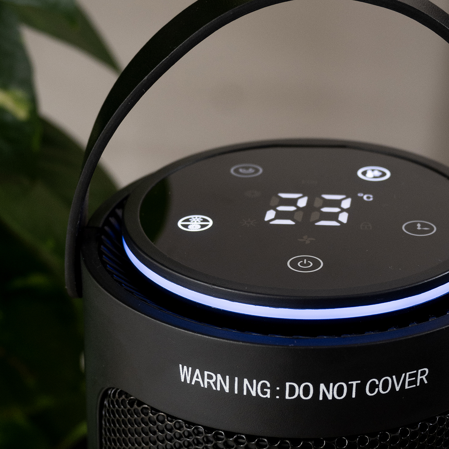 Close-up of a black electric heater with digital display showing 23 degrees Celsius. It has a handle and warning text.