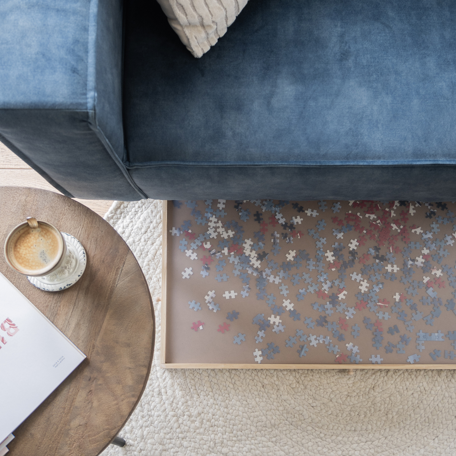 A top-down view shows a blue sofa, a coffee table with coffee, and a puzzle on a tray under the sofa. A white rug is present.