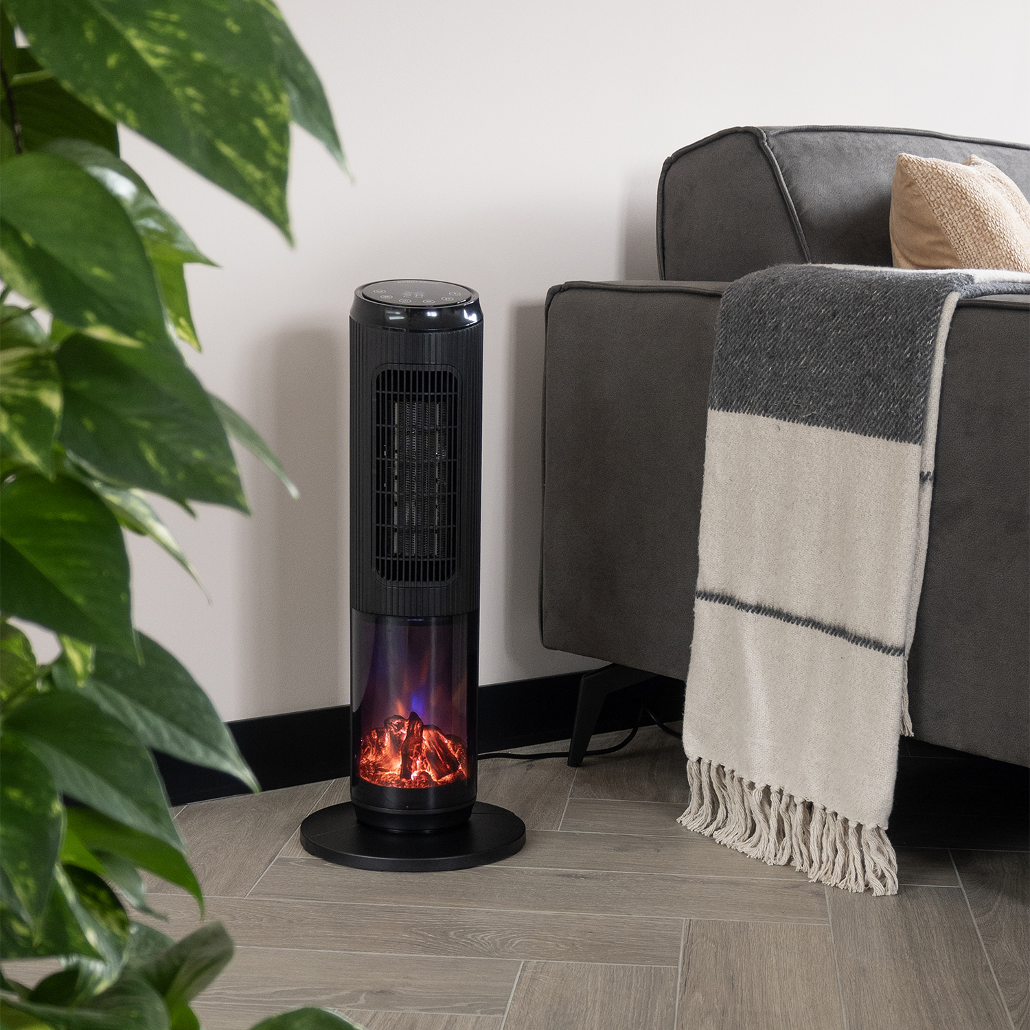 A black electric fireplace is next to a gray sofa. A blanket is draped over the sofa. Green plant leaves are in the foreground.