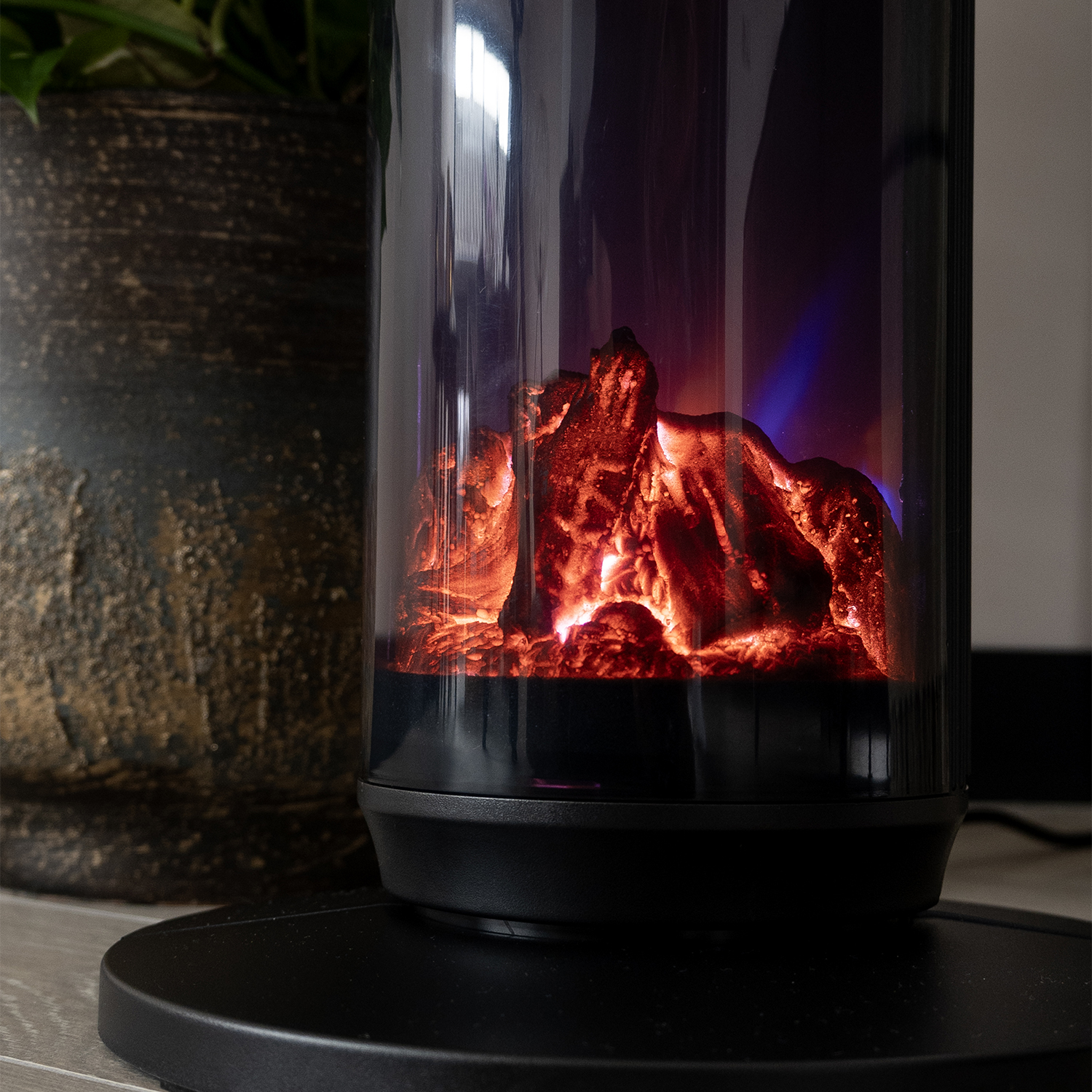 A decorative electric fireplace with a simulated fire effect. A potted plant is in the background.