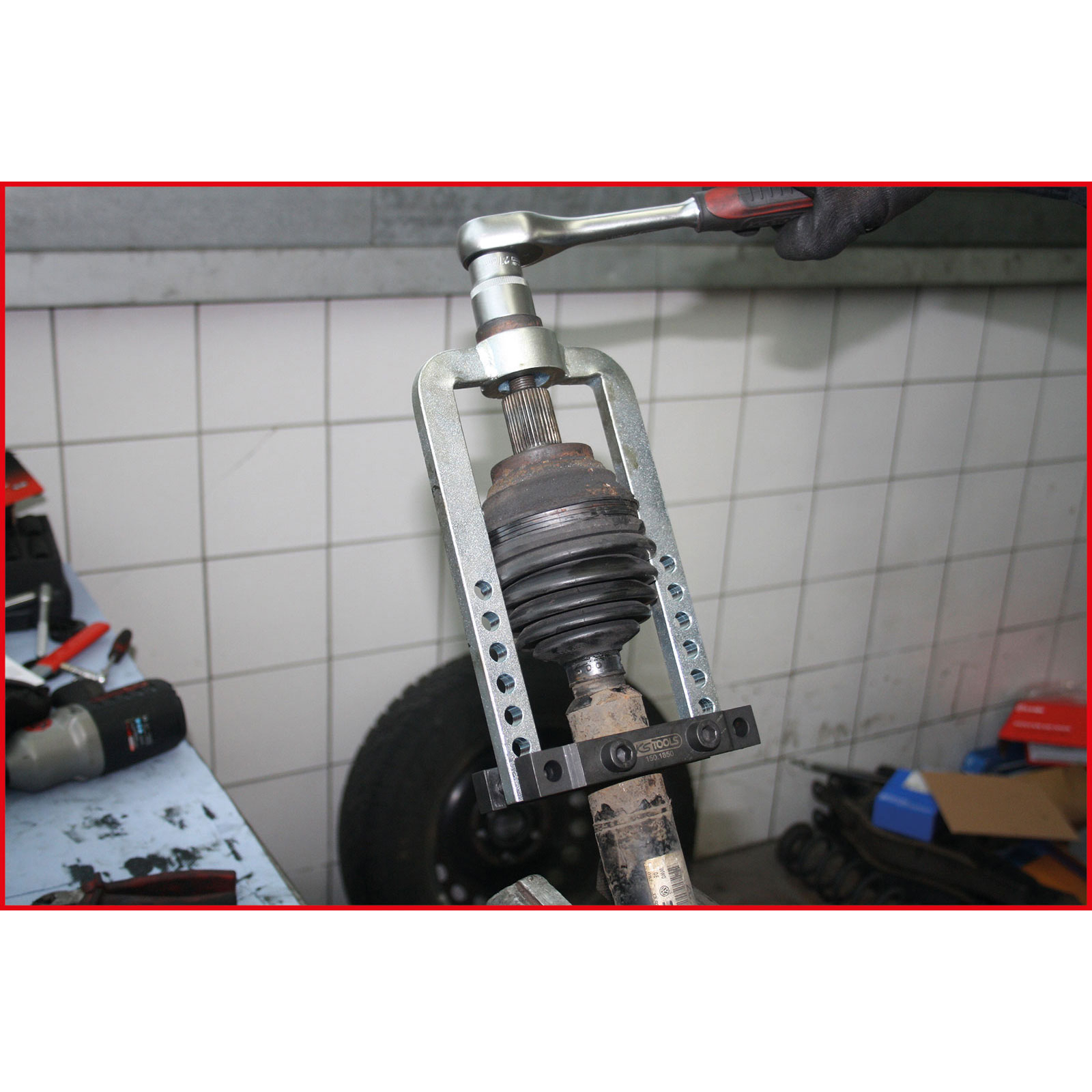 Ein Mechaniker verwendet ein Werkzeug, um ein Autoteil zu entfernen. Das Teil wird von einem Metallrahmen gehalten, eine Ratsche wird verwendet.