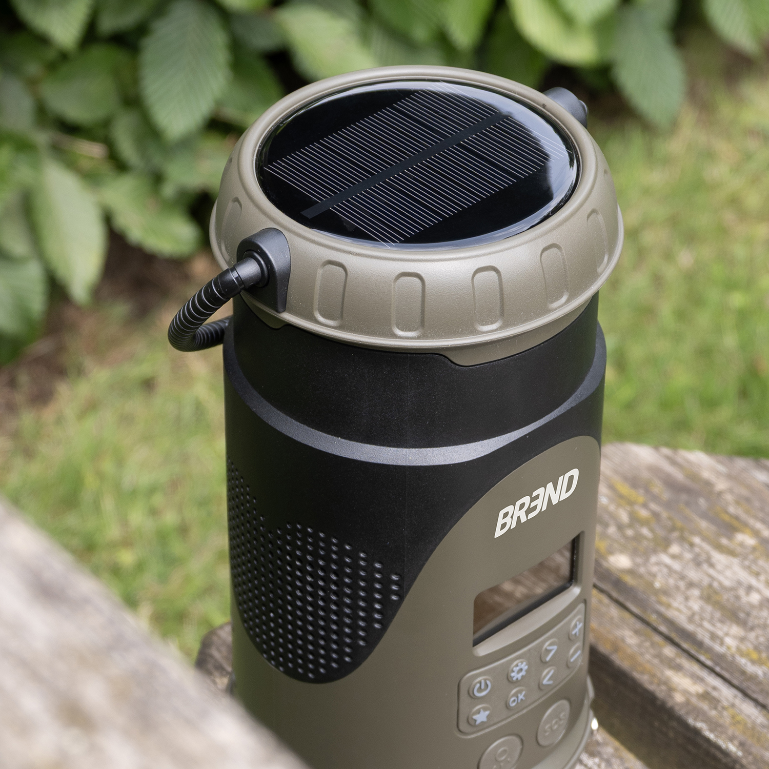 A solar-powered device with a black top and a screen, sitting on a wooden bench. Green foliage is in the background.