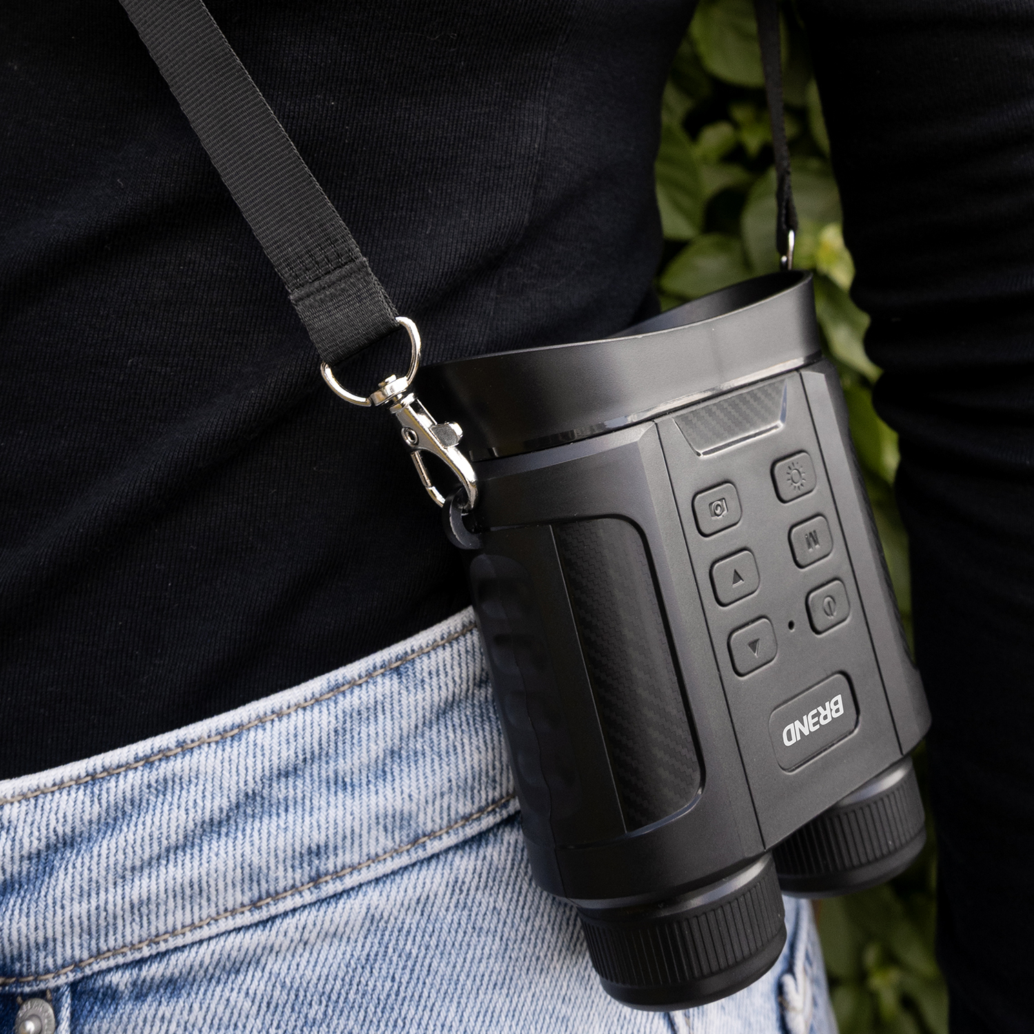 Une personne en chemise noire et jean porte un appareil de vision nocturne noir. L'appareil est suspendu à une sangle.