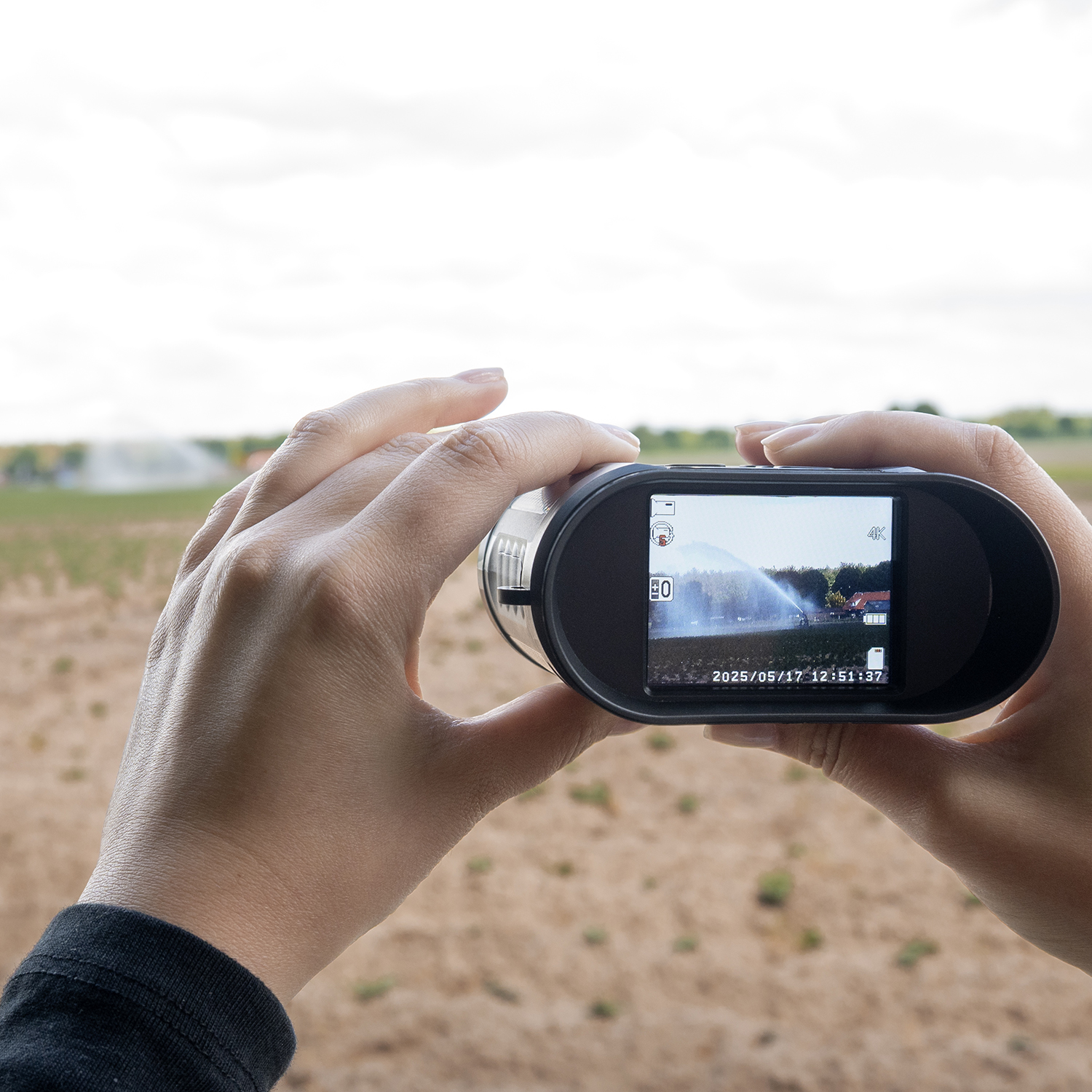 Mains tenant une caméra vidéo, montrant un champ arrosé. L'écran de la caméra affiche la scène avec la date et l'heure.