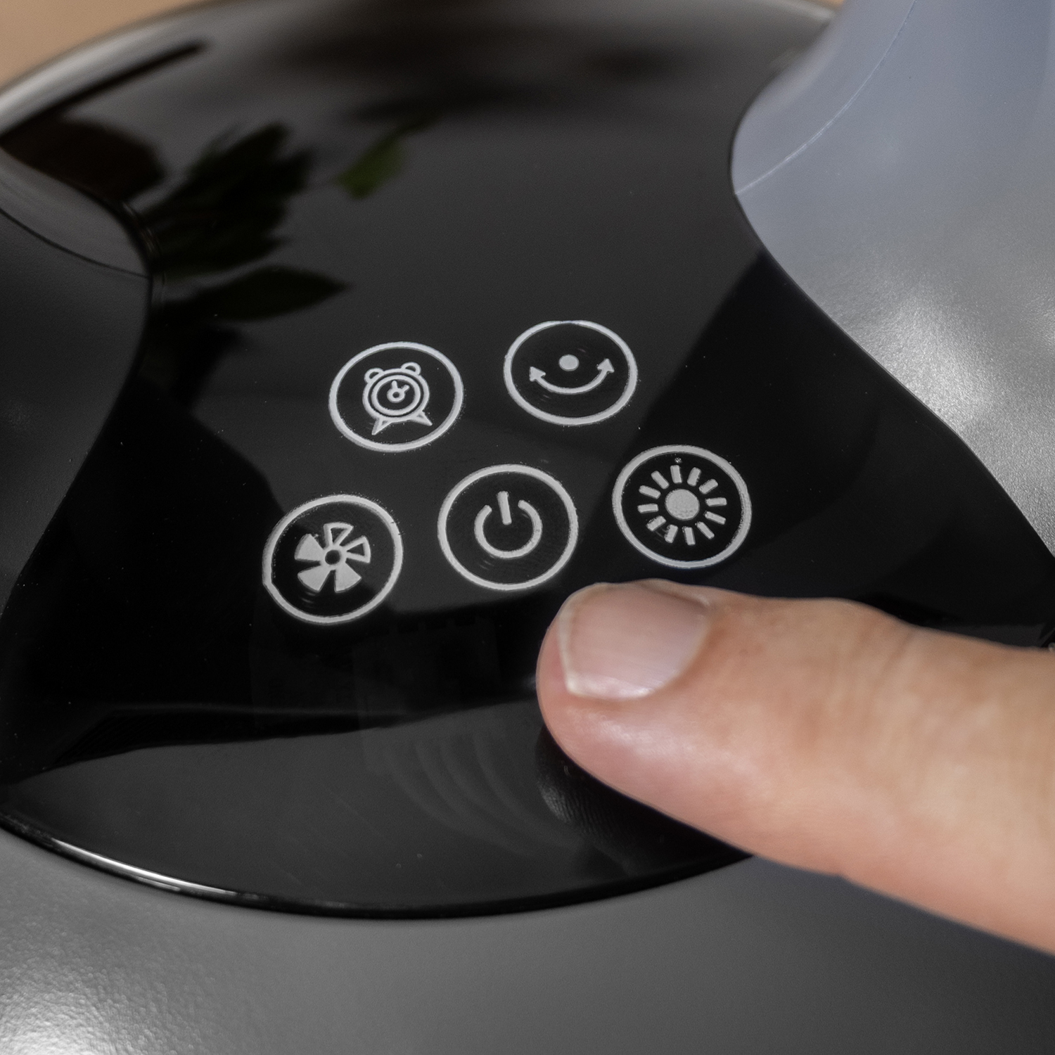 Een hand drukt op een knop op een zwart bedieningspaneel van een ventilator. Knoppen zijn onder meer aan/uit, ventilator, timer en modusinstellingen.