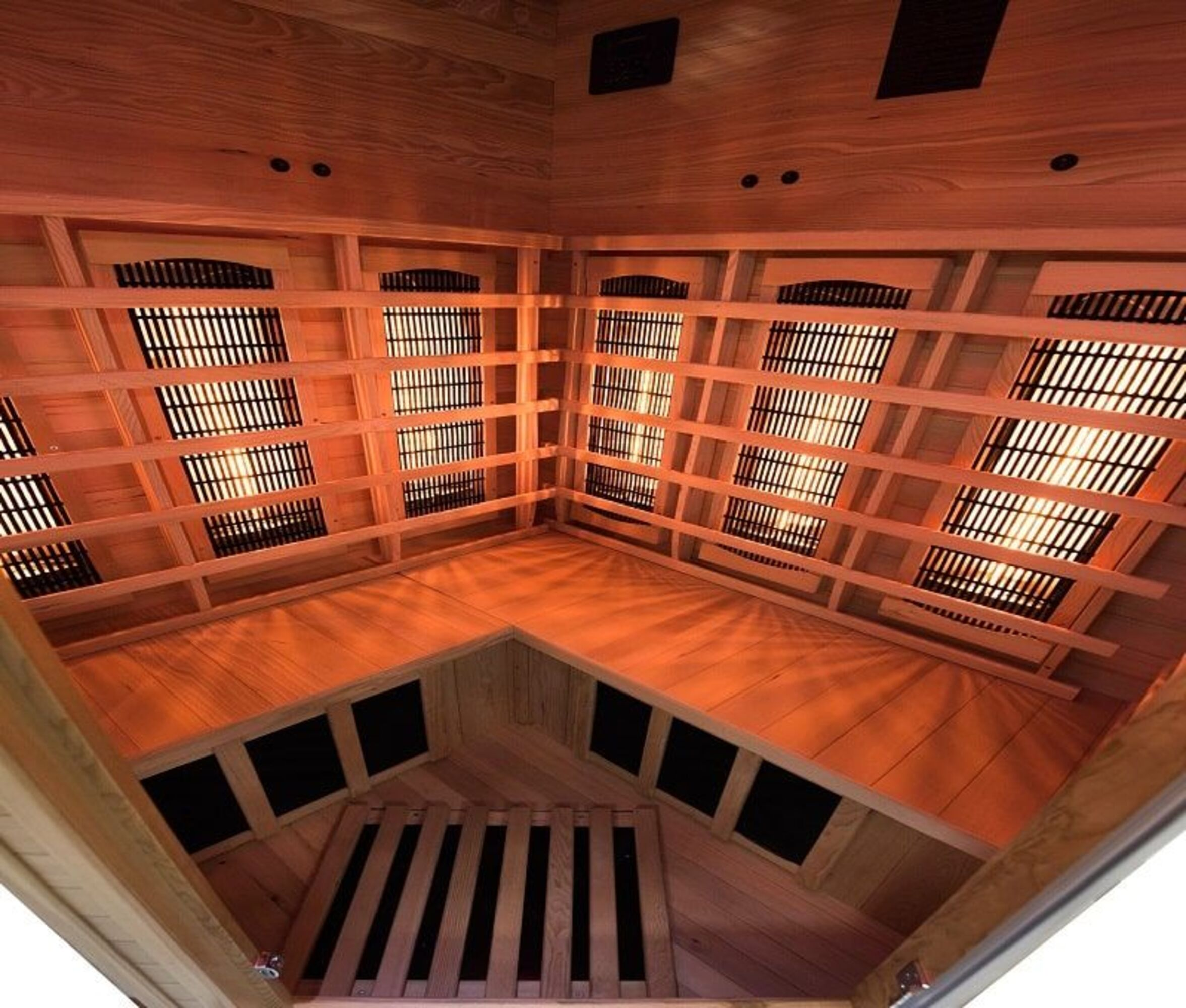 Interior de sauna de madera. Tiene bancos, paneles infrarrojos y ventilaciones. La iluminación es cálida y naranja.