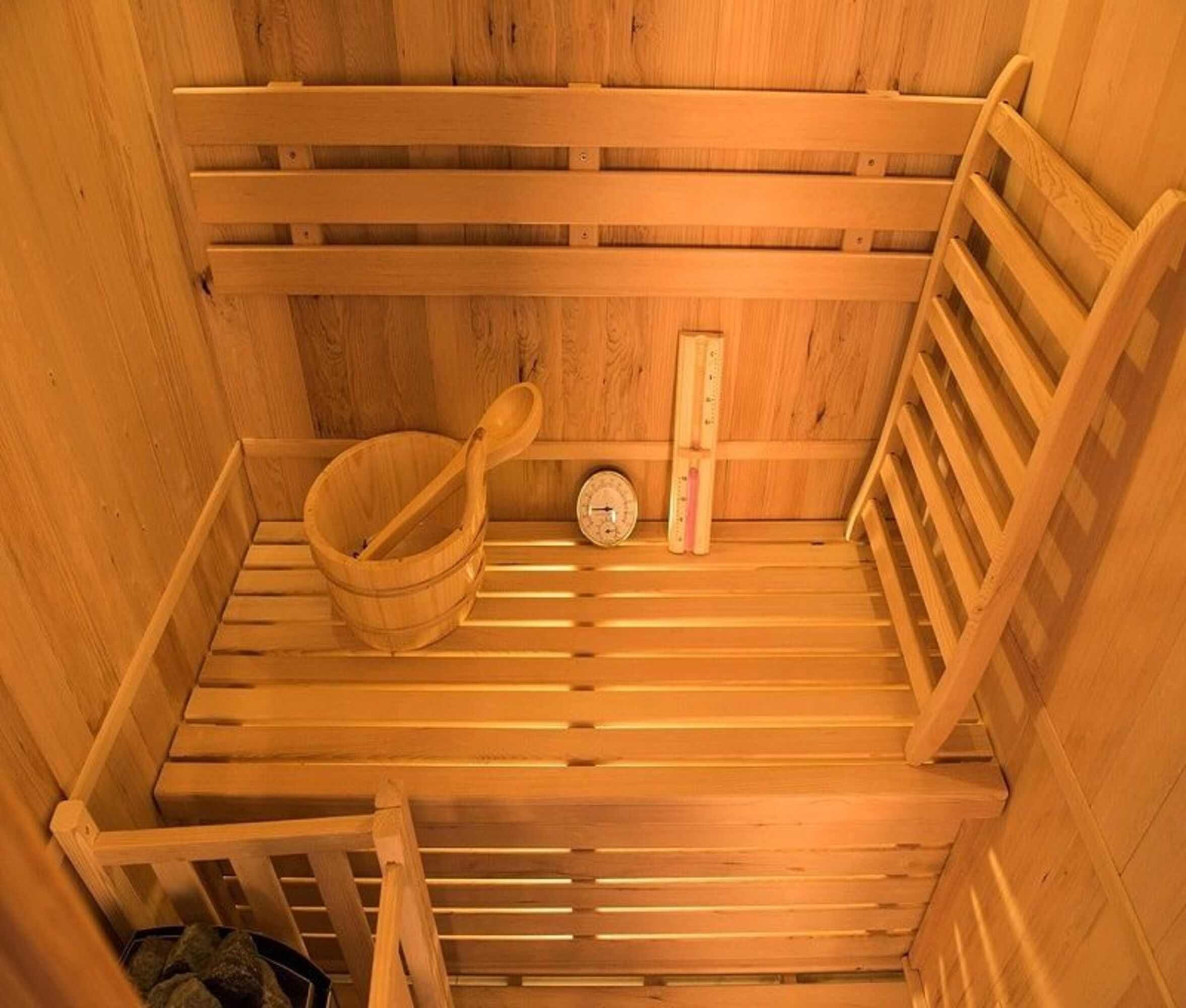 Interior de sauna de madera. Incluye bancos, un cubo con un cucharón, un termómetro y un medidor de temperatura. Las paredes son de madera.