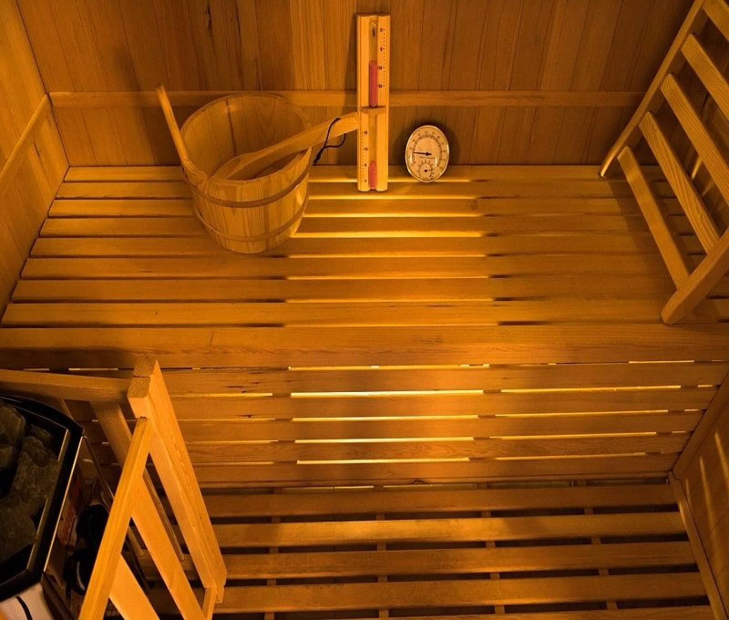 Interior de sauna de madera con banco, cubo, termómetro y reloj.