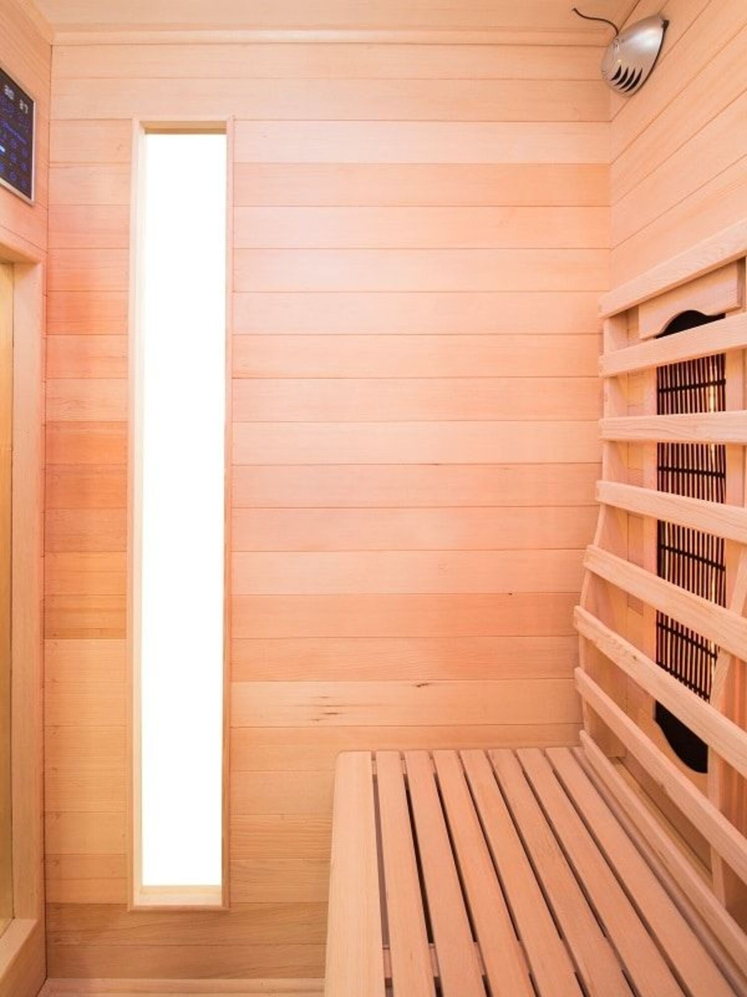Interior de sauna de madera con banco, ventana y elemento calefactor. Paneles de madera clara cubren paredes y techo.