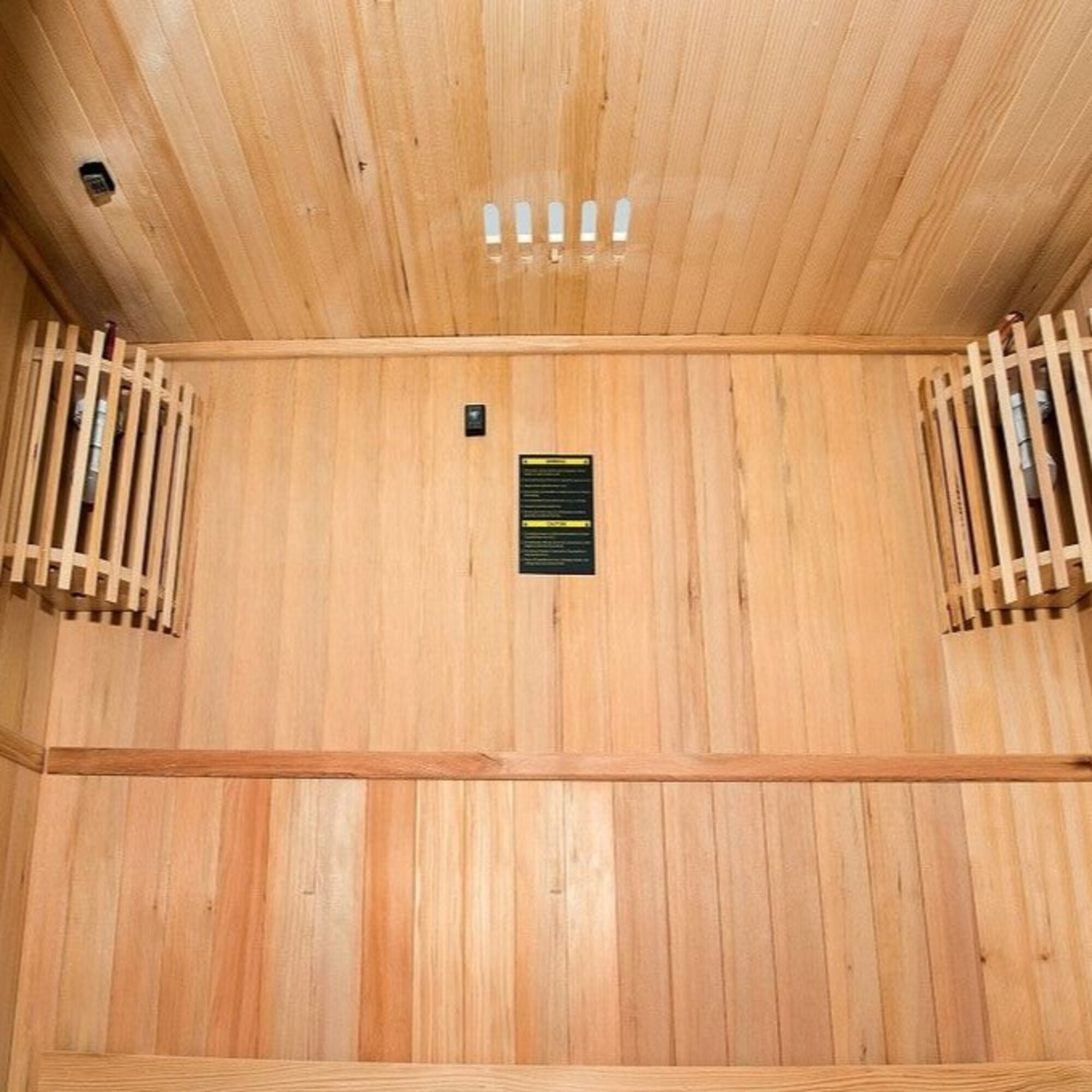 Interior de una sauna de madera con techo, paredes y ventilaciones de color claro. Dos estructuras de madera cuelgan en las paredes laterales.