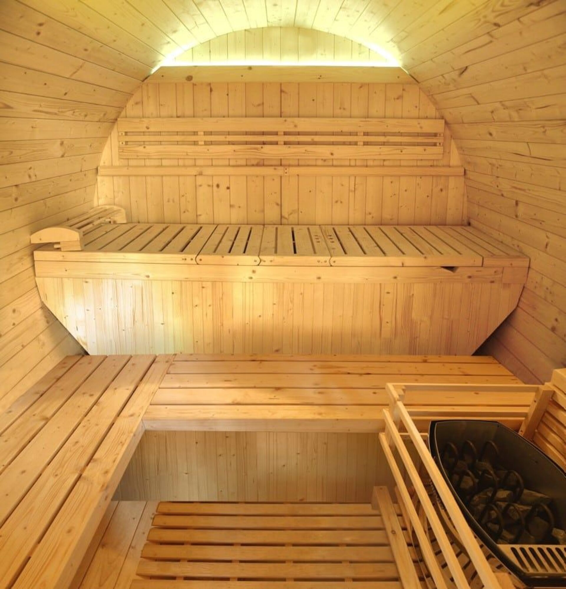Vista interior de una sauna de madera con bancos y un calentador. La sauna es de madera clara.