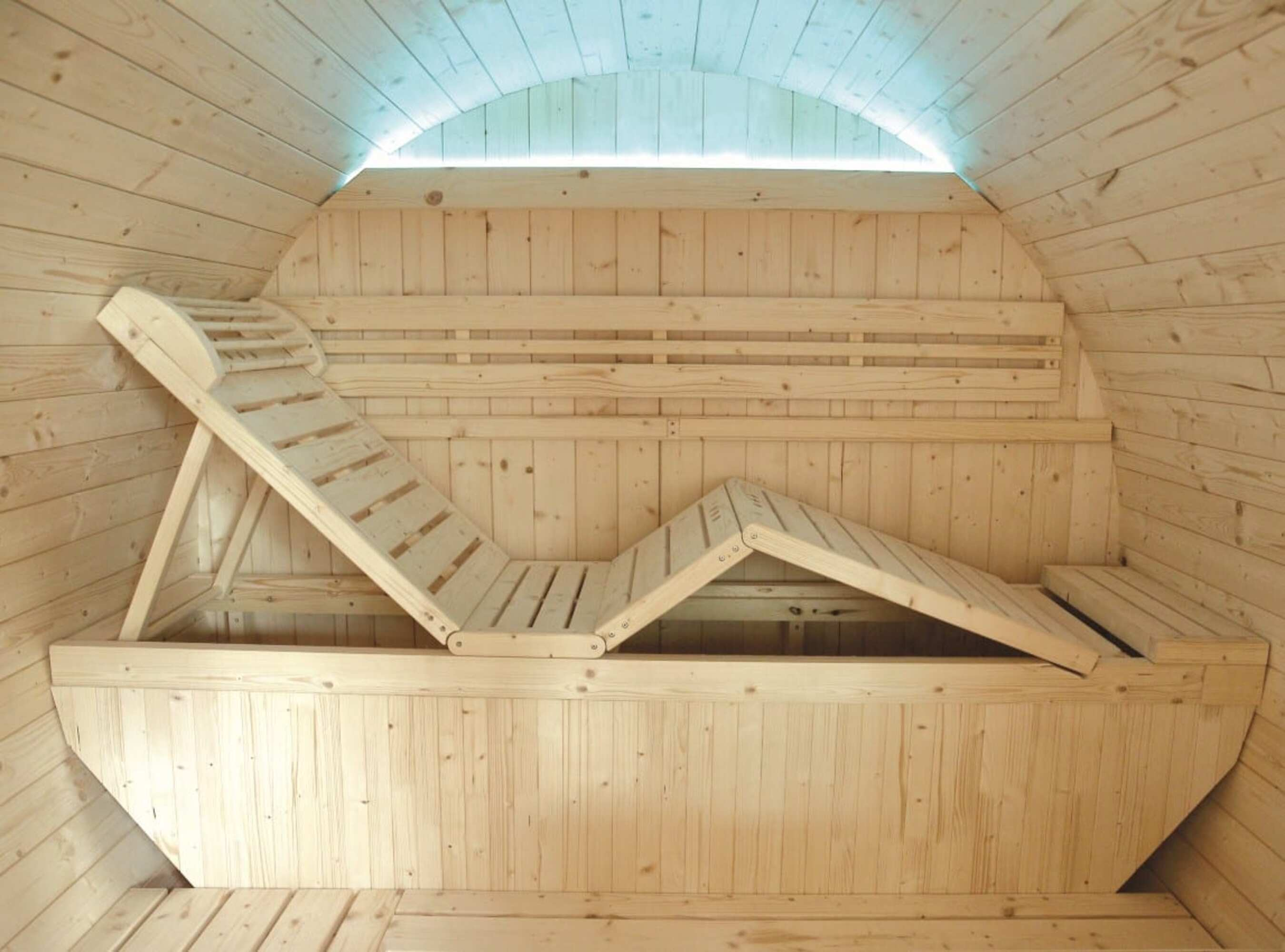 Interior de sauna de madera con banco reclinado. Las paredes y el techo son de madera.