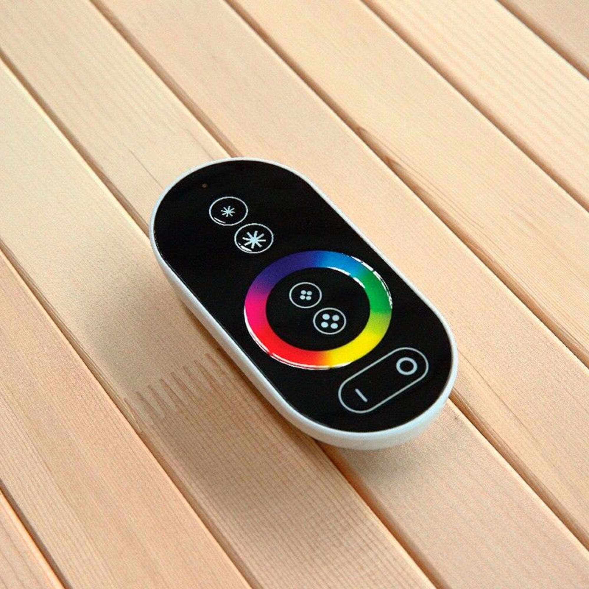 Un mando a distancia blanco y negro con botones coloridos, sobre una superficie de madera.