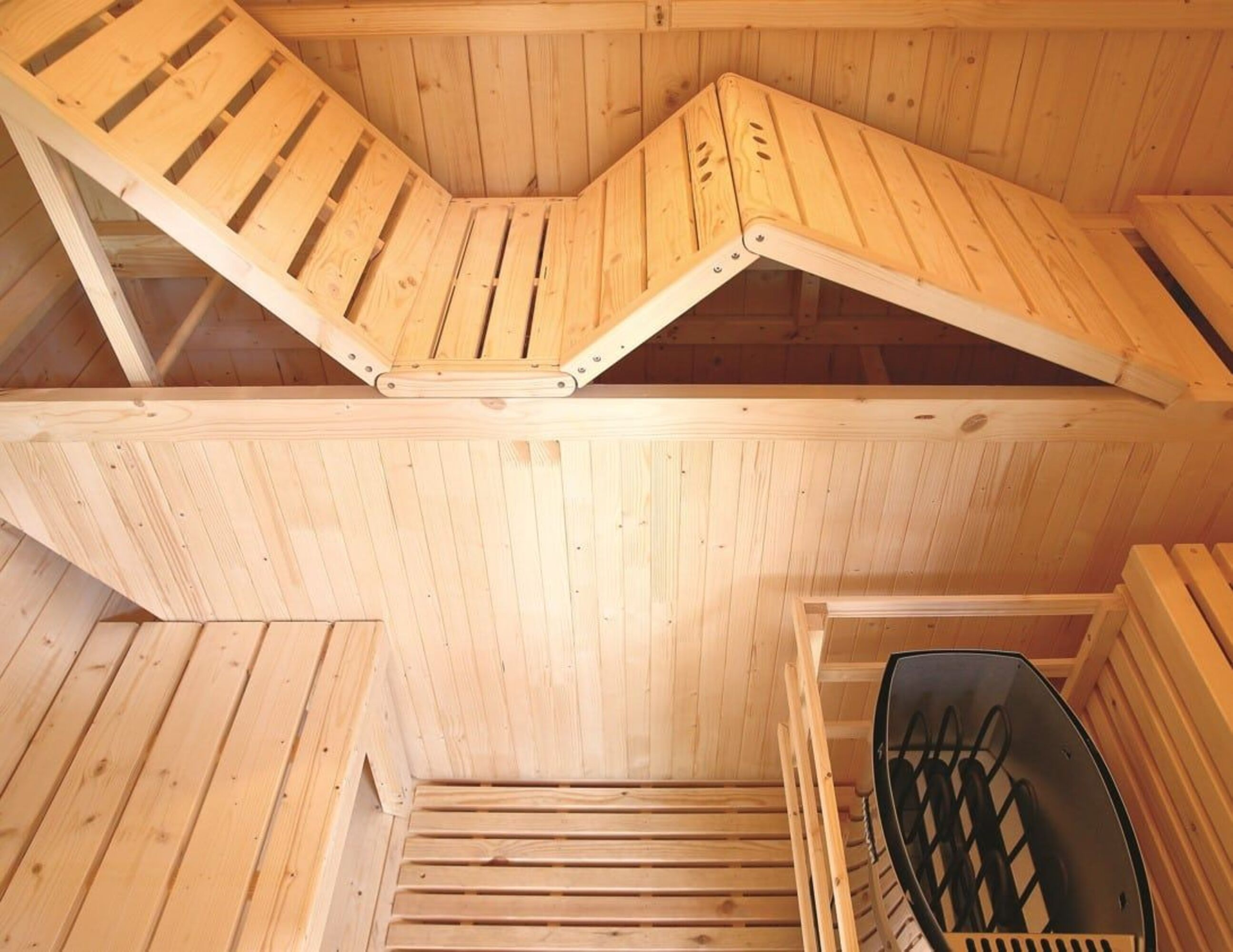 Interior de sauna de madera con bancos de listones, zona de estar en ángulo y un calentador negro. Predomina la madera clara.