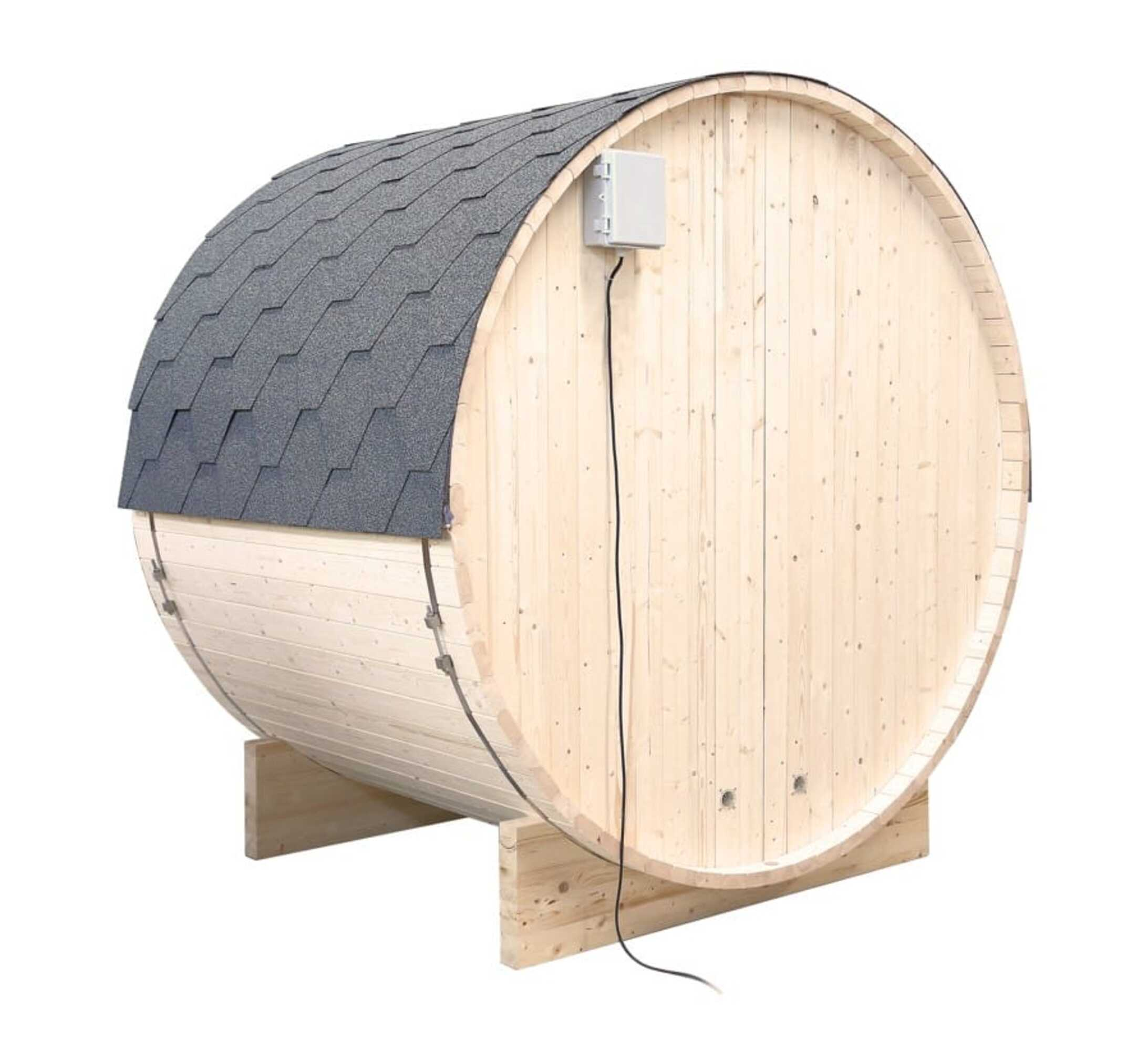 Una sauna de barril de madera con techo de tejas grises, una caja blanca y un cable negro. Está sobre soportes de madera sobre un fondo blanco.