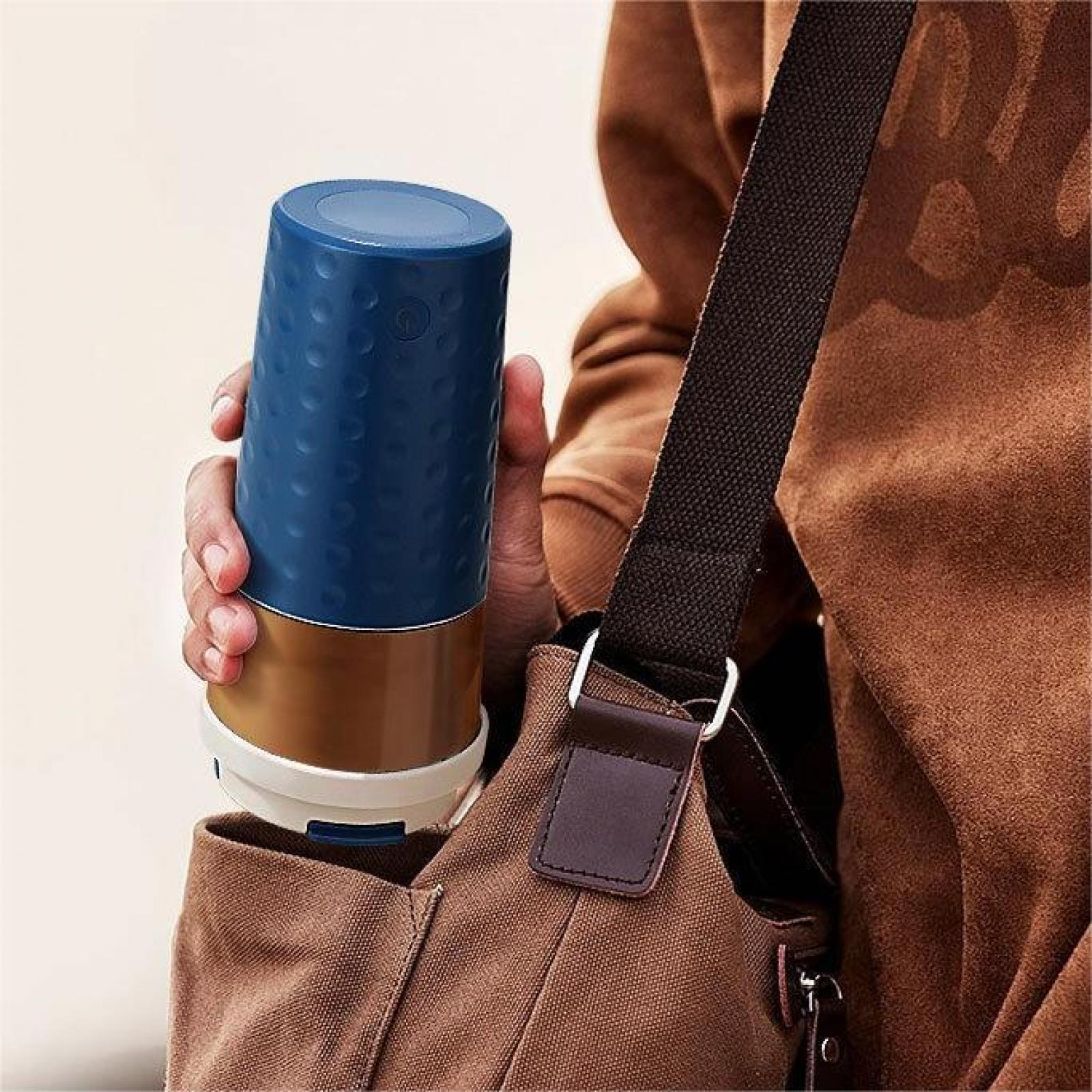 Eine Person hält einen blau-braunen Reisebecher. Eine braune Tasche mit schwarzem Gurt hängt über der Schulter.