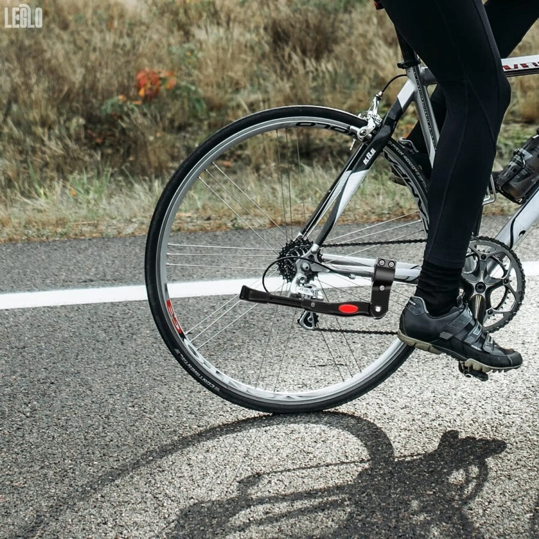 Ein Radfahrer fährt auf einer Straße mit dem Fahrrad. Das Fahrrad hat einen schwarzen Rahmen, der Fahrer trägt schwarze Hosen und Schuhe.
