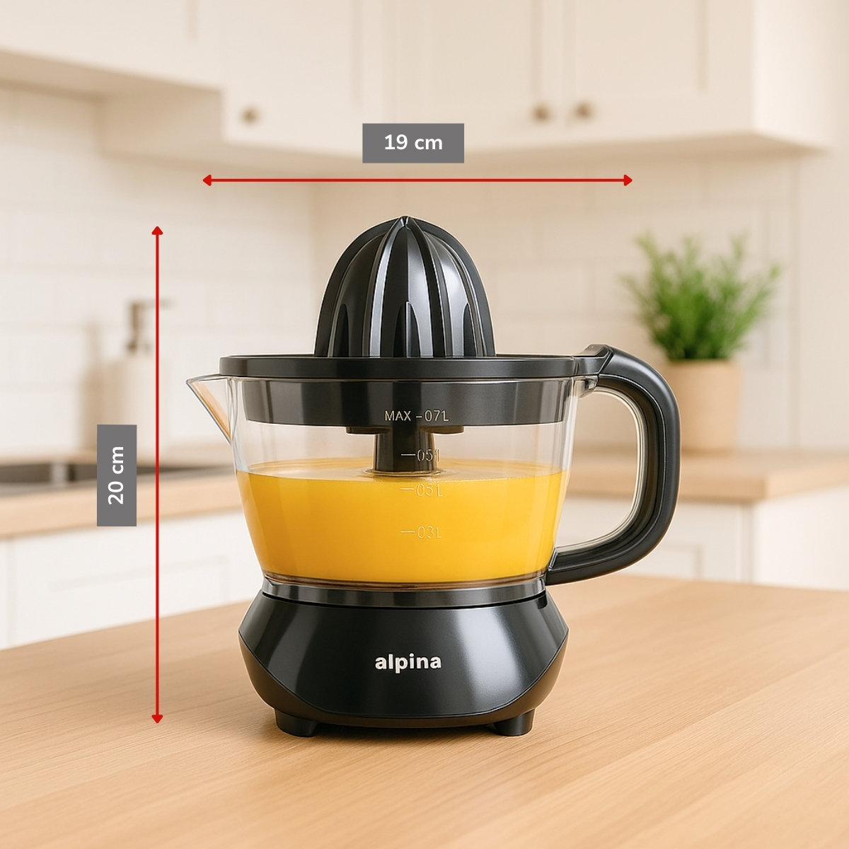 A black and clear juicer with orange juice inside. The juicer is on a wooden table. A plant is in the background.