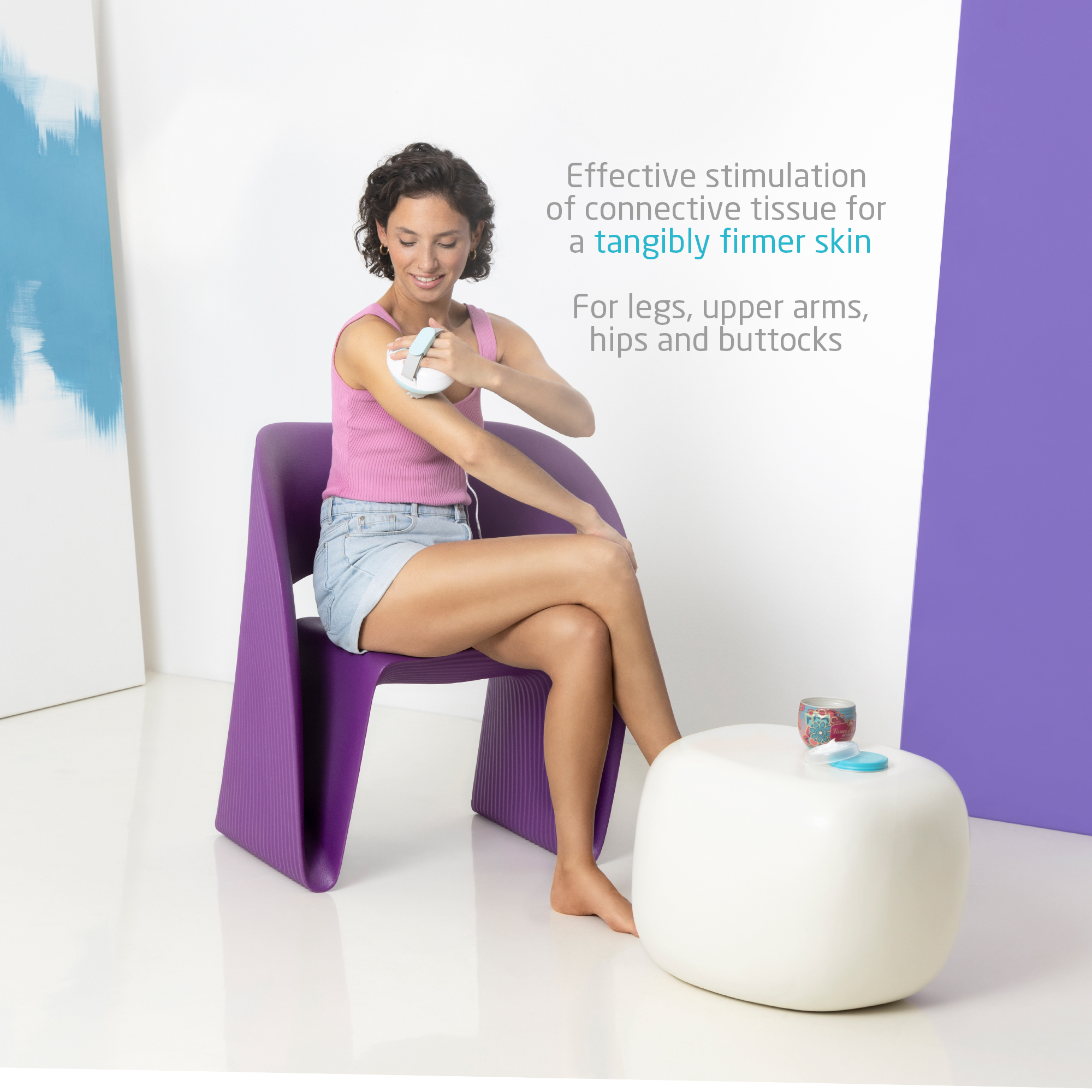 Kobieta używająca urządzenia do masażu na ramieniu, siedząca na fioletowym krześle. Biały stół z puszką i niebieską nakrętką.