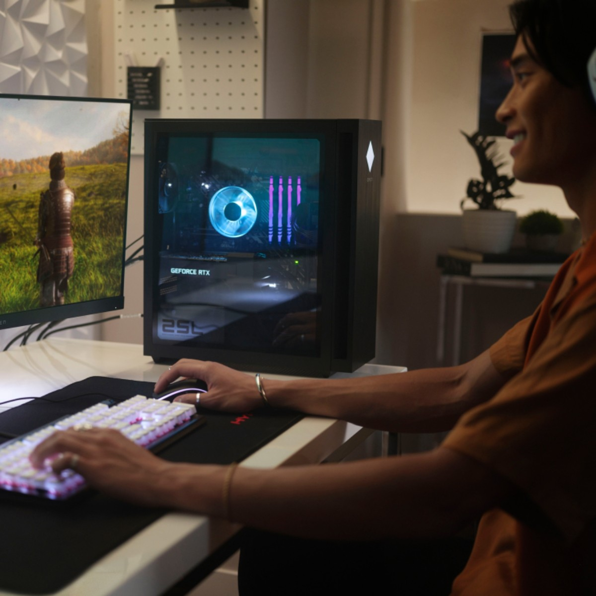Un uomo sta giocando. Un PC è sulla scrivania. Un monitor mostra un paesaggio. La tastiera e il mouse sono illuminati. L'uomo sorride.