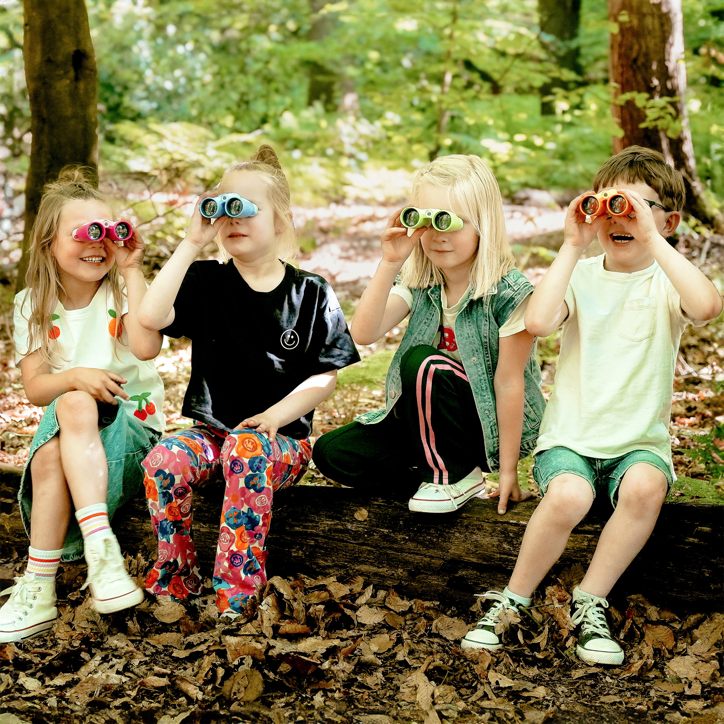 Vier Kinder auf einem Baumstamm, die im Wald Ferngläser benutzen. Sie sind verschiedenen Alters und tragen bunte Kleidung.
