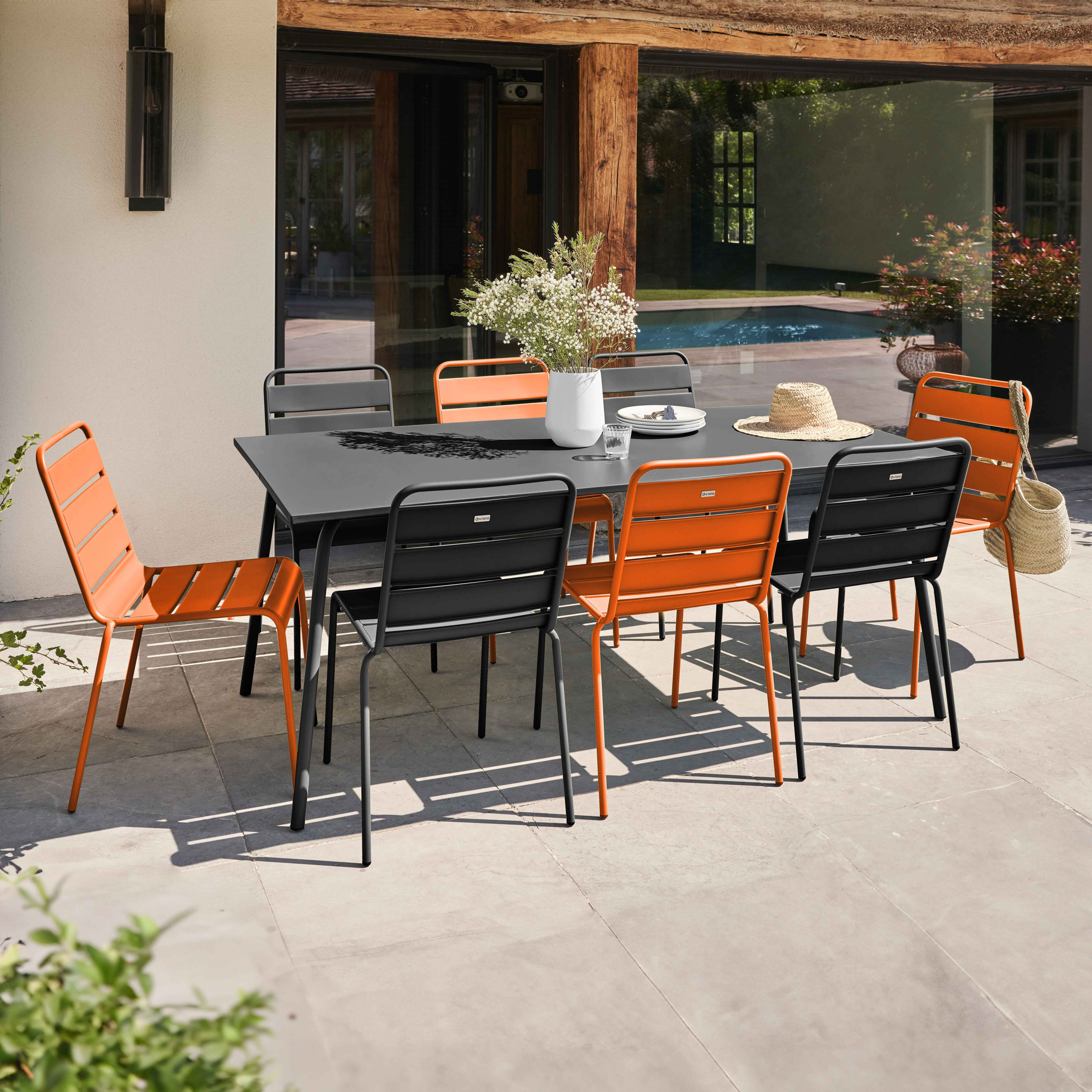 Terrasse mit dunklem Tisch, Stühlen und einer weißen Vase mit Blumen. Strohhut auf dem Tisch.