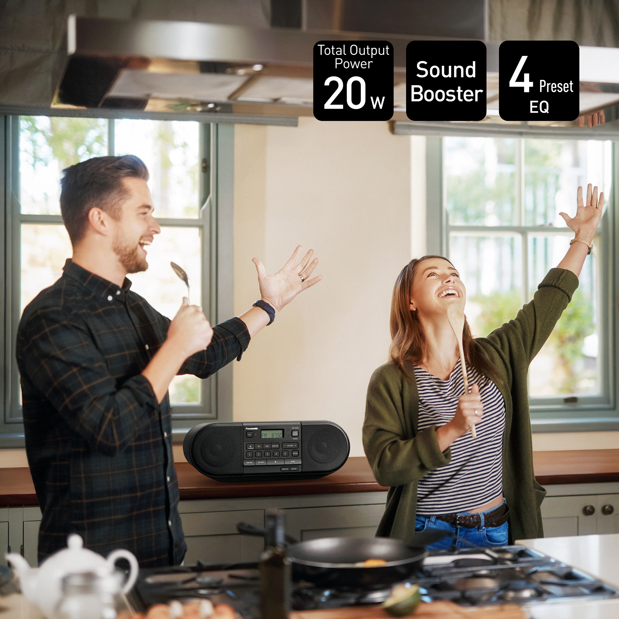 Una coppia canta con cucchiai in cucina. Un altoparlante è sul bancone. In alto c'è scritto 'Total Output Power 20W'.
