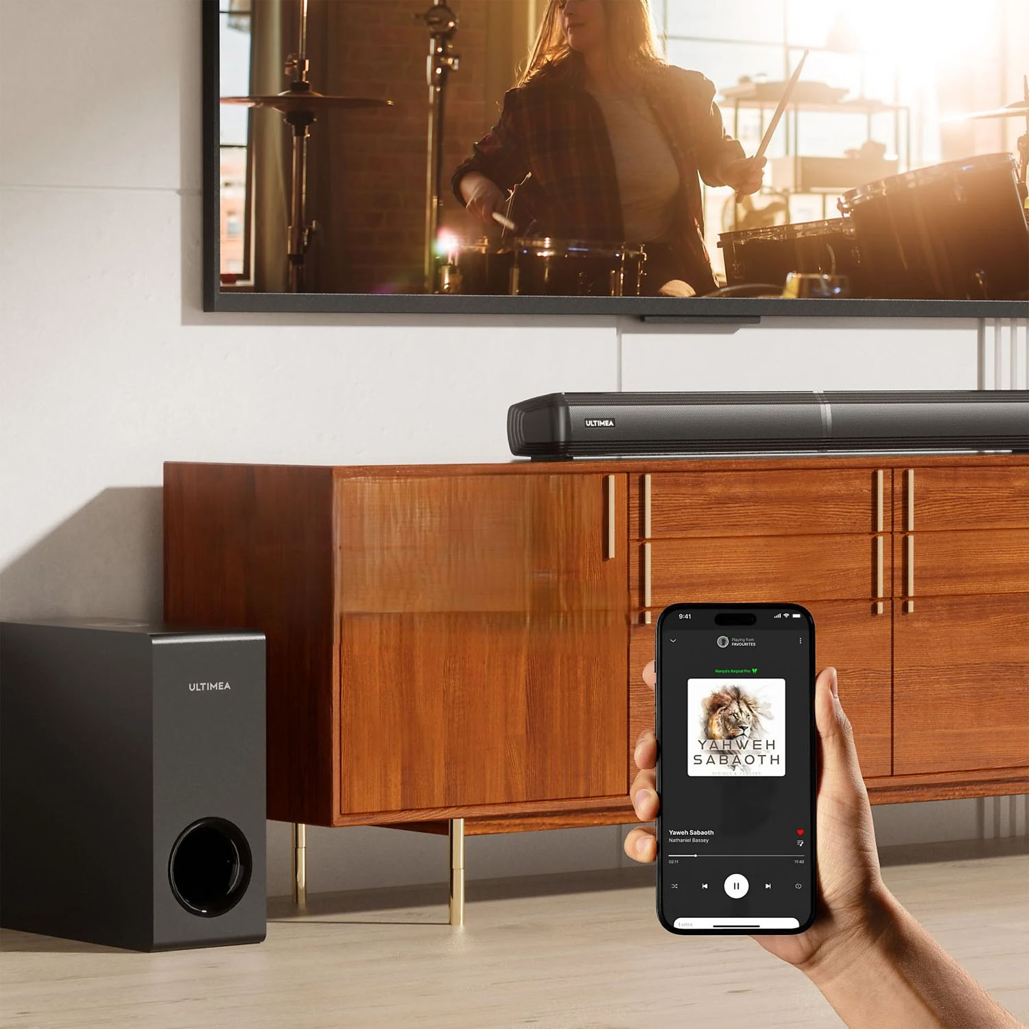 Osoba trzymająca telefon z muzyką. Soundbar i subwoofer przed drewnianą szafką. Telewizor pokazuje perkusistę.