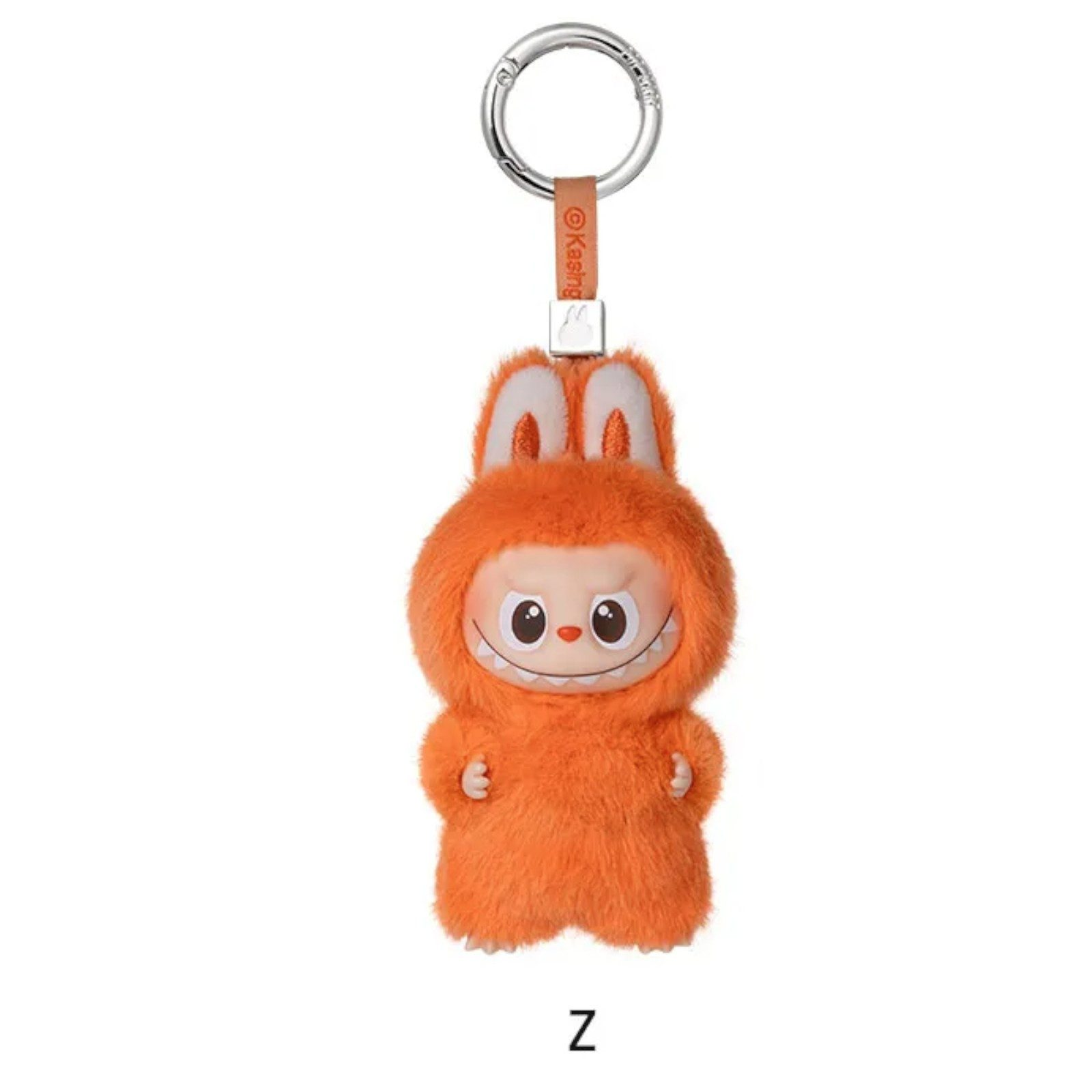 Ein orangefarbener Plüschtier-Schlüsselanhänger in Form eines Monsters mit einem lächelnden Gesicht, mit Metallring und braunem Riemen.