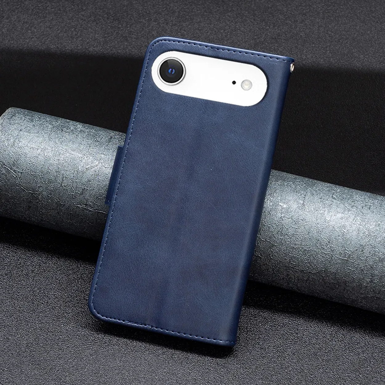 Een blauwe leren telefoonhoes met een witte camera-uitsparing ligt op een getextureerd oppervlak. Een grijs, opgerold materiaal staat op de achtergrond.