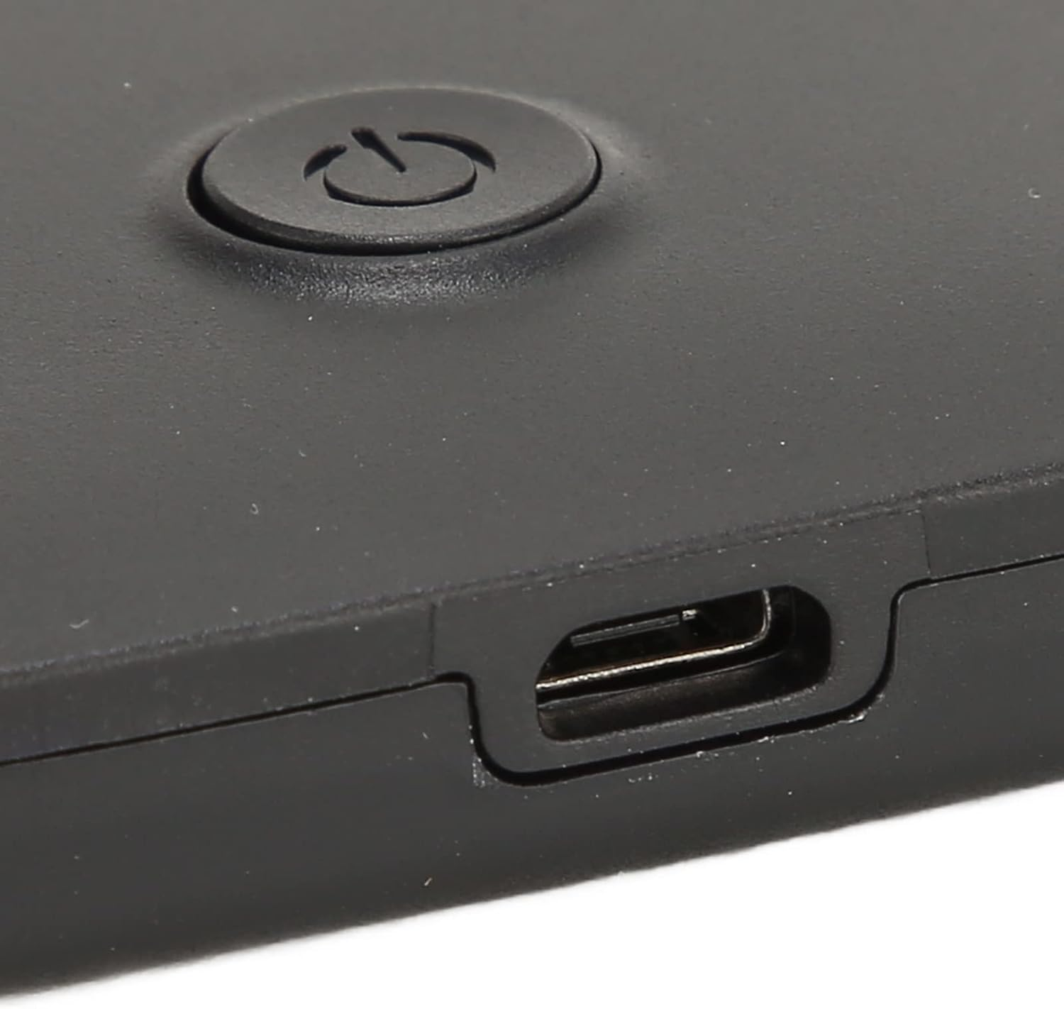 Nahaufnahme eines schwarzen Geräts. Sichtbar sind ein Einschaltknopf und ein USB-Anschluss. Die Oberfläche ist matt und leicht strukturiert.