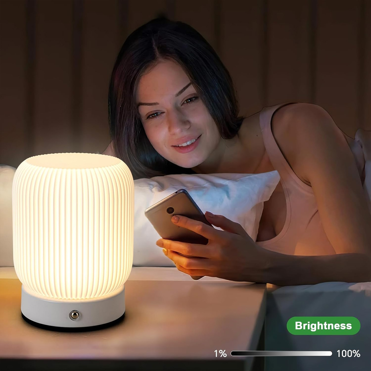 Eine Frau im Bett benutzt ein Telefon neben einer leuchtenden Lampe. Der Helligkeitsregler zeigt 100 %. Die Szene ist schwach beleuchtet.
