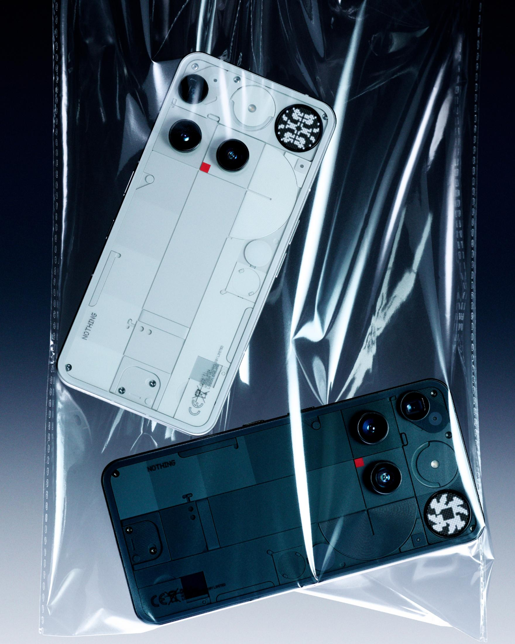 Dwa smartfony, jeden biały, drugi ciemnoszary, w przezroczystej plastikowej torbie. Telefony mają widoczne elementy i obiektywy.