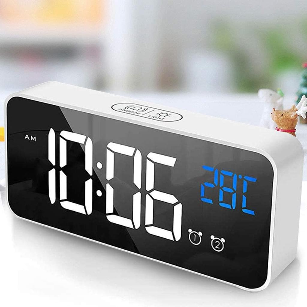 Ein weißer digitaler Wecker, der 10:06 Uhr und 28 °C anzeigt. Er hat ein schwarzes Display und einen weißen Rahmen mit Tasten.