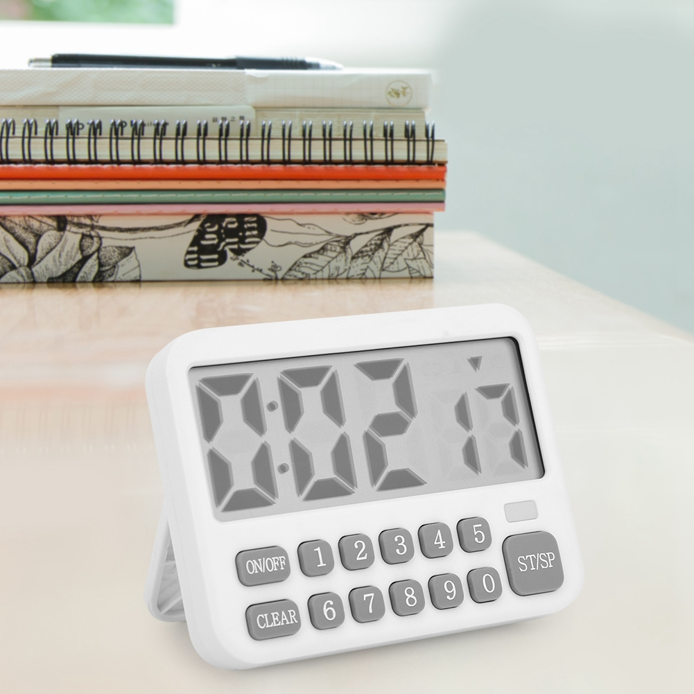 Ein weißer digitaler Küchentimer zeigt 0:02:17 an. Er hat Knöpfe und steht auf einem Tisch mit gestapelten Notizbüchern im Hintergrund.