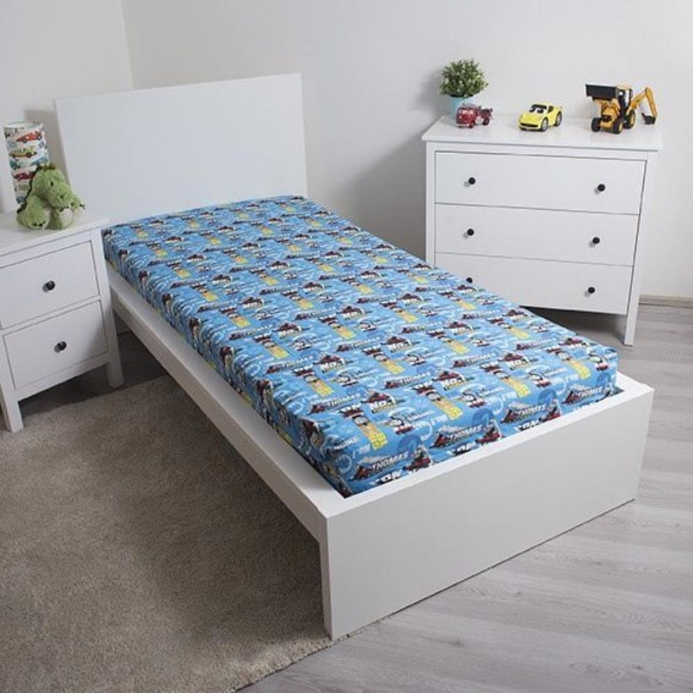 Ein Kinderzimmer mit weißem Bett, blau gemusterter Bettwäsche, weißen Möbeln und Spielzeugautos auf einer Kommode. Ein grünes Spielzeug steht auf einem Nachttisch.