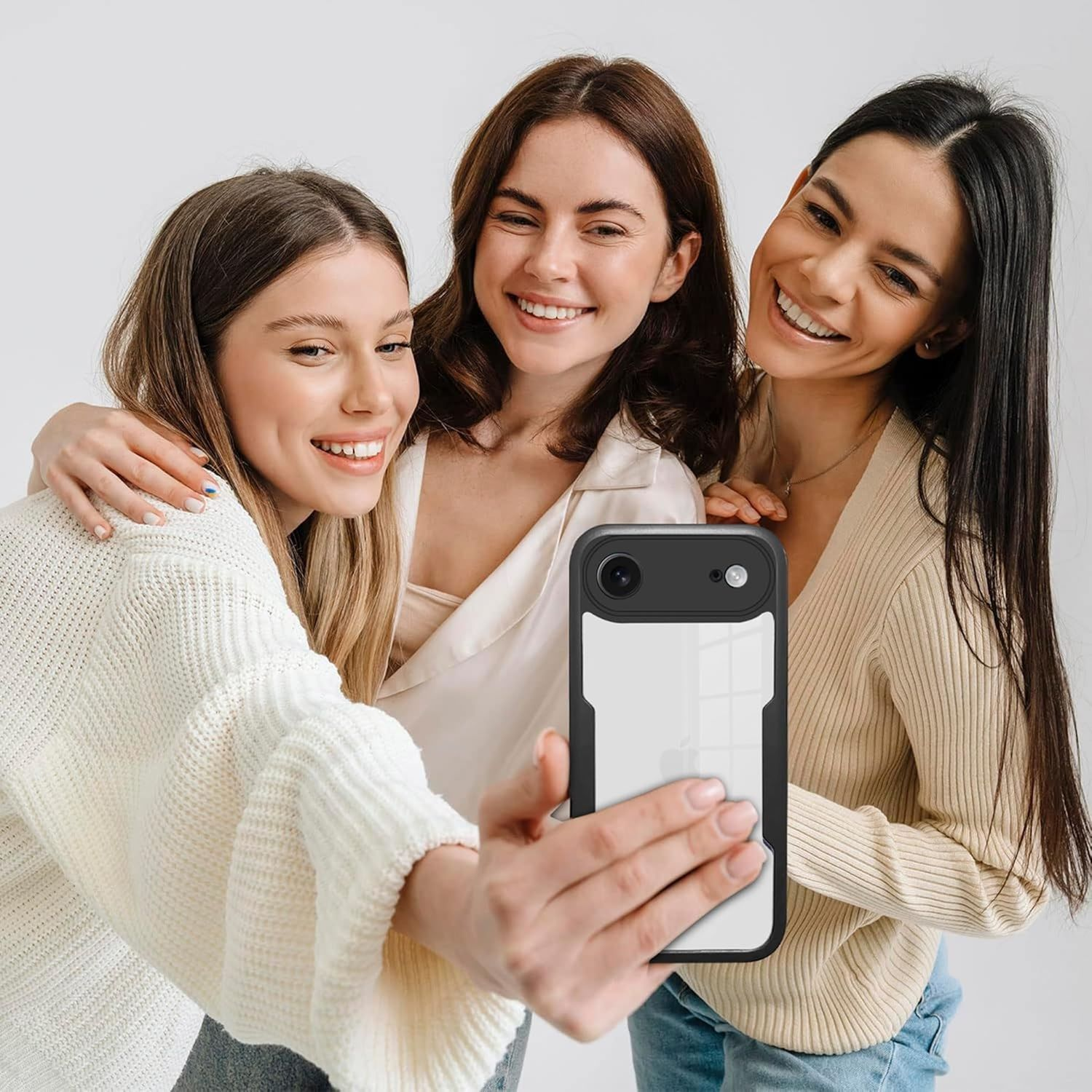 Drei lächelnde Frauen machen ein Selfie mit einem Telefon. Eine hält das Telefon. Weißer Hintergrund.