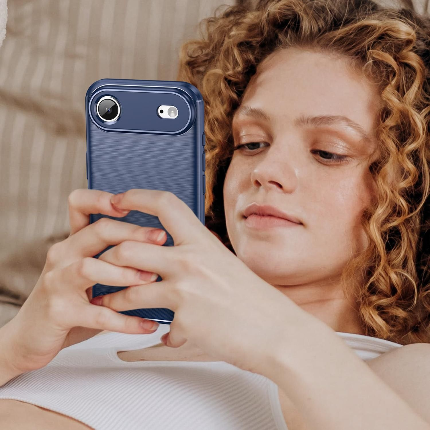 Eine Frau mit lockigem Haar betrachtet ein Telefon in einer blauen Hülle. Sie hält das Telefon mit beiden Händen.