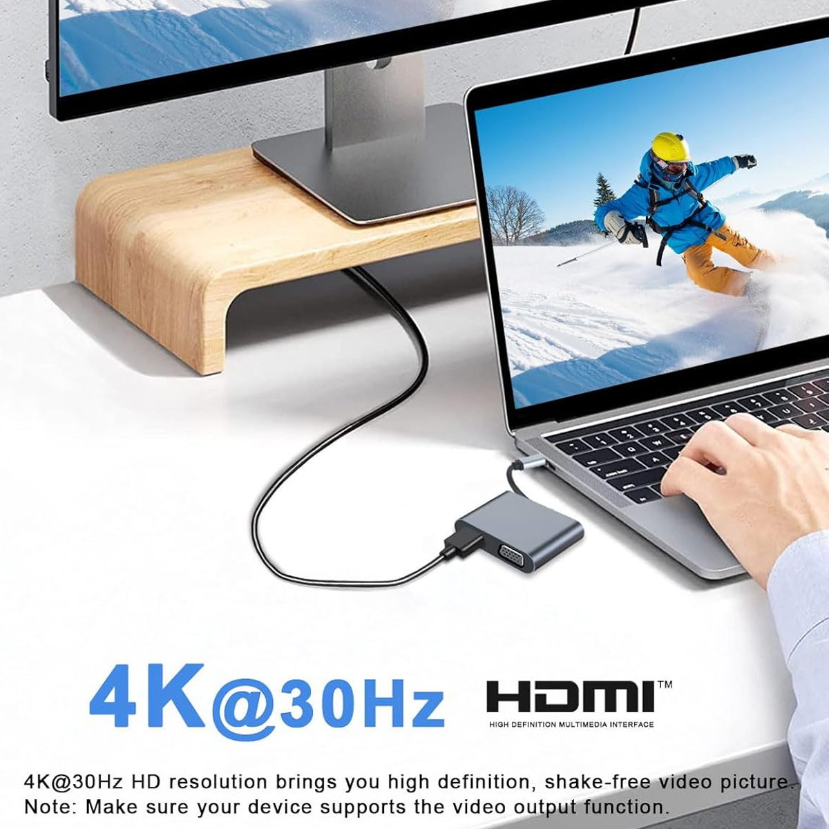 Laptop, Monitor und Konverter verbunden. Bildschirm zeigt Skifahrer. 4K@30Hz HDMI Logo. Weißer Schreibtisch mit Holzständer.