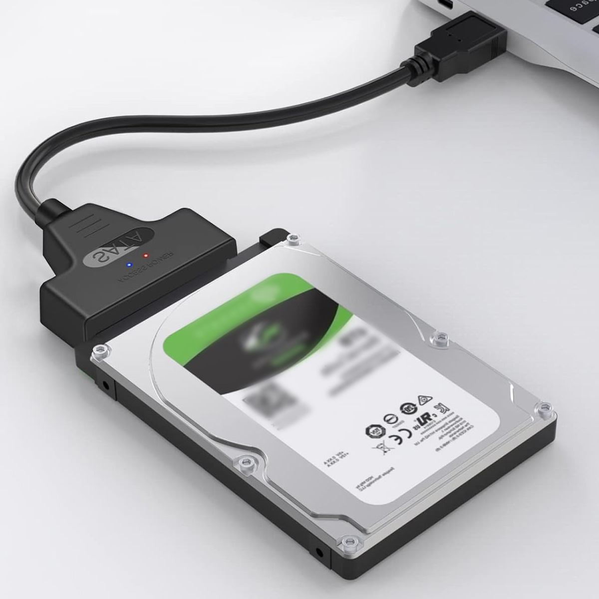Eine Festplatte, die über ein schwarzes SATA-zu-USB-Kabel mit einem Laptop verbunden ist. Das Laufwerk ist silber und schwarz, mit einem grünen Etikett.